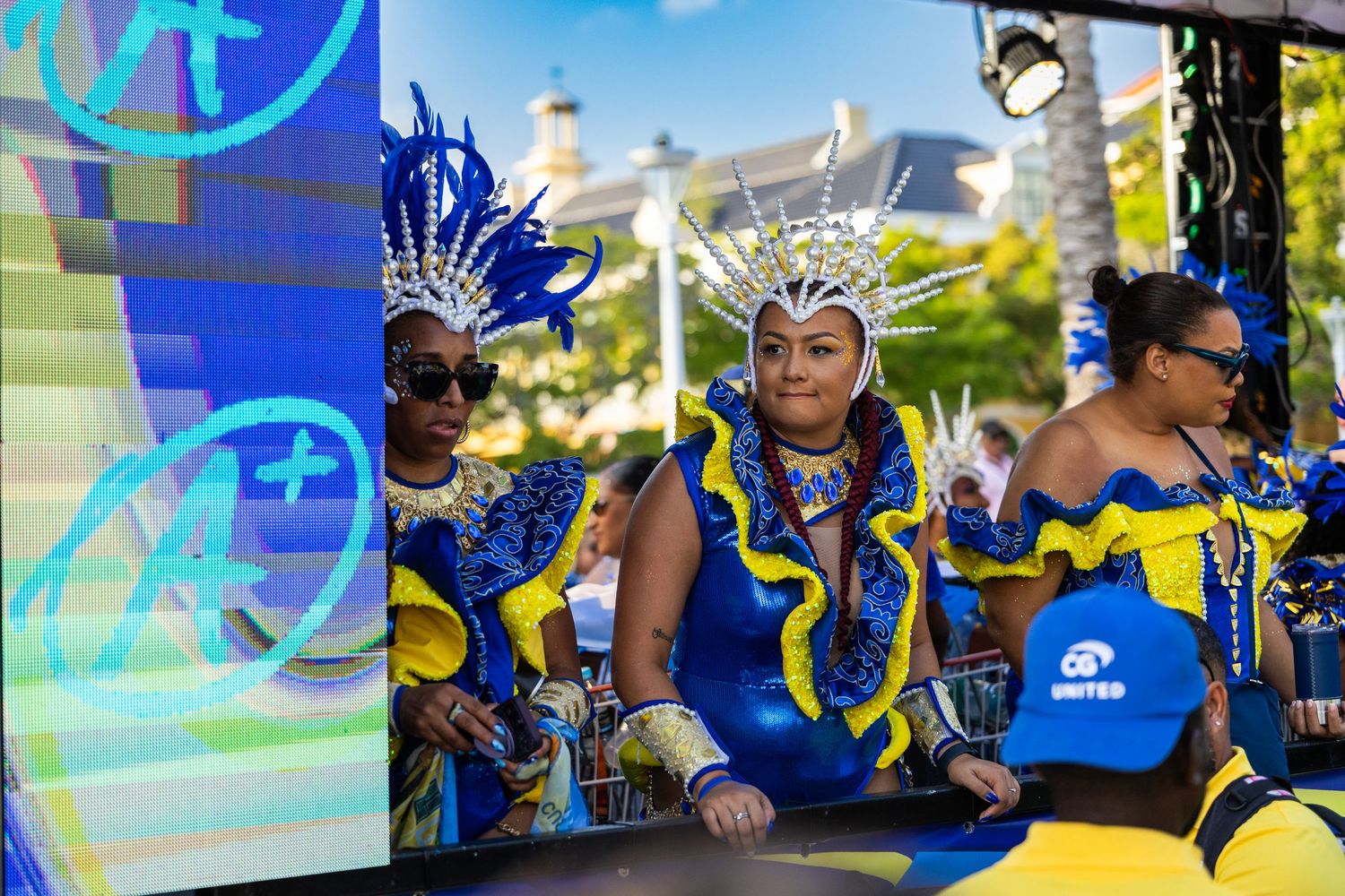 Festival performers in bright blue and yellow costumes dance against digital display screens.