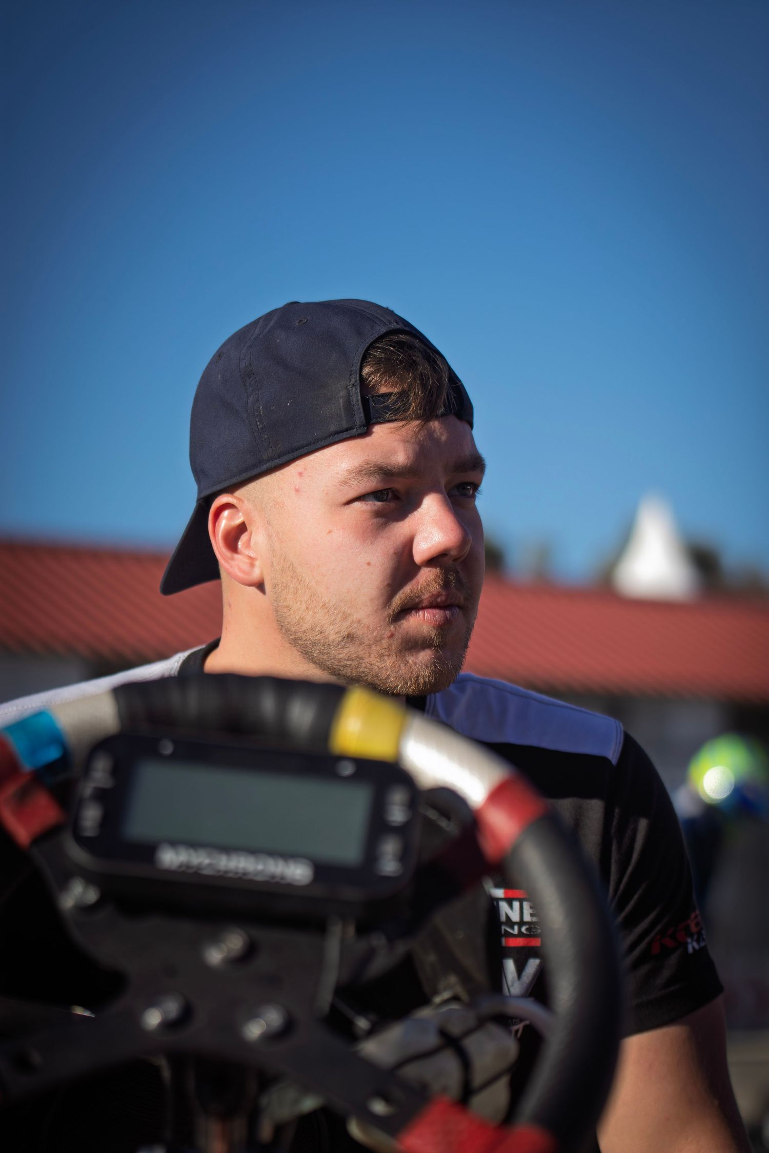 Close-up profile of race car drivers wearing baseball caps against blue sky.