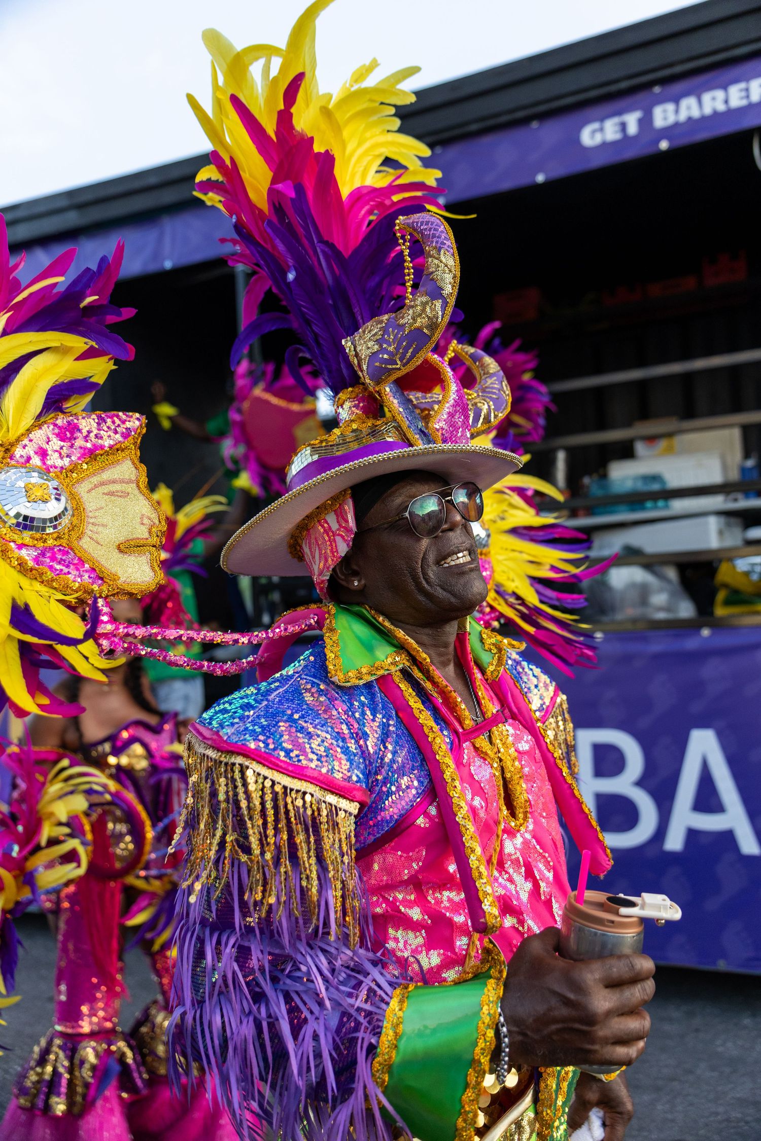 Carnival performers in purple and yellow feathered headdresses dance during a festival parade.