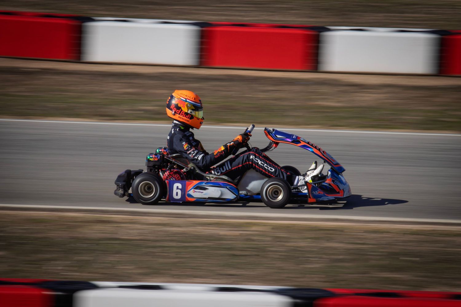 Go-karts racing on a track with red and white barriers in the background.
