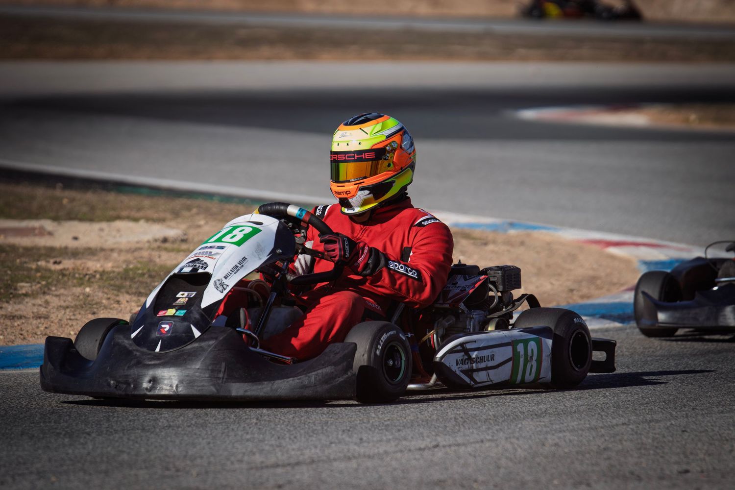 Go-karts racing on an outdoor track with drivers in racing gear.