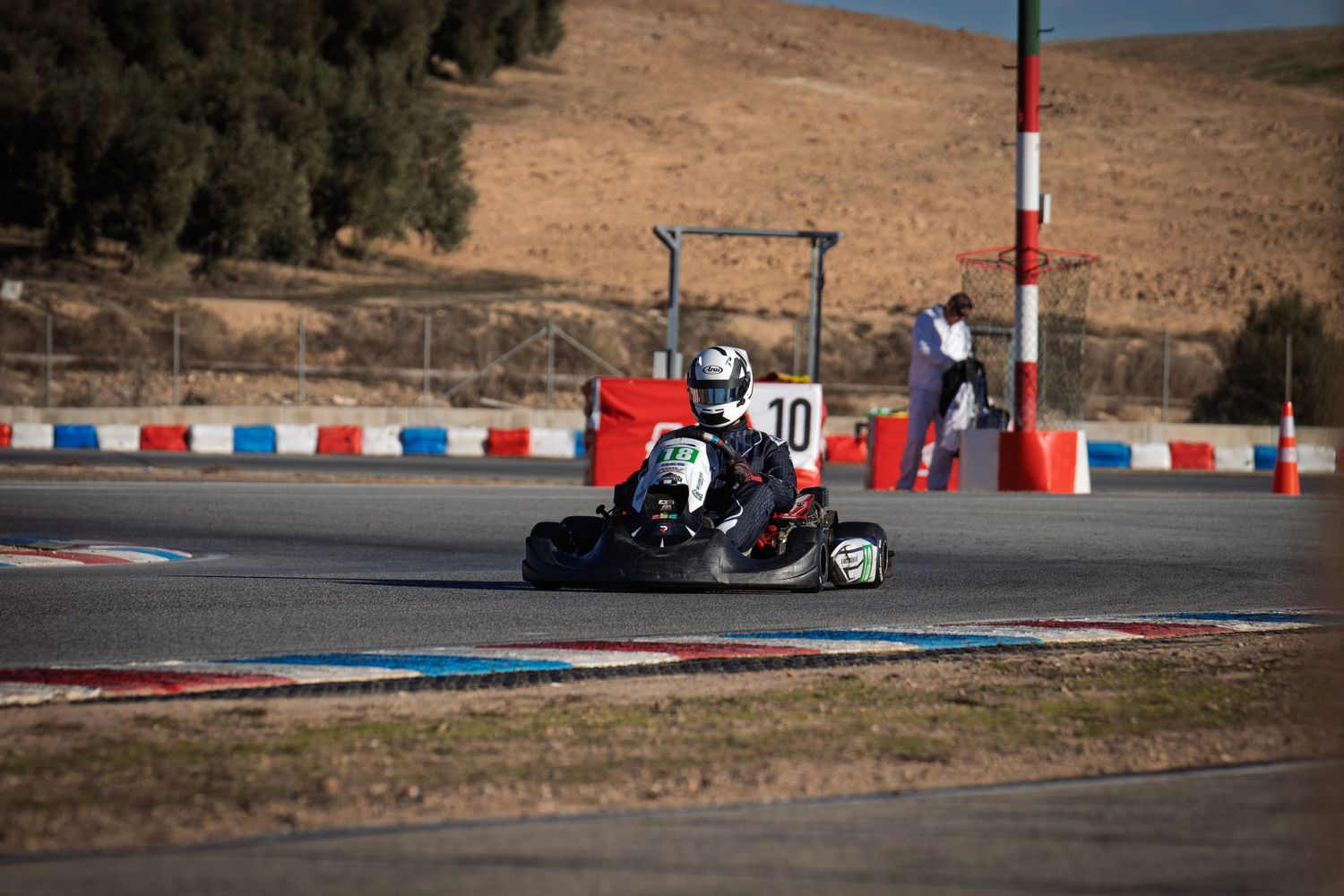Go-kart races past red and blue track barriers on a desert circuit.