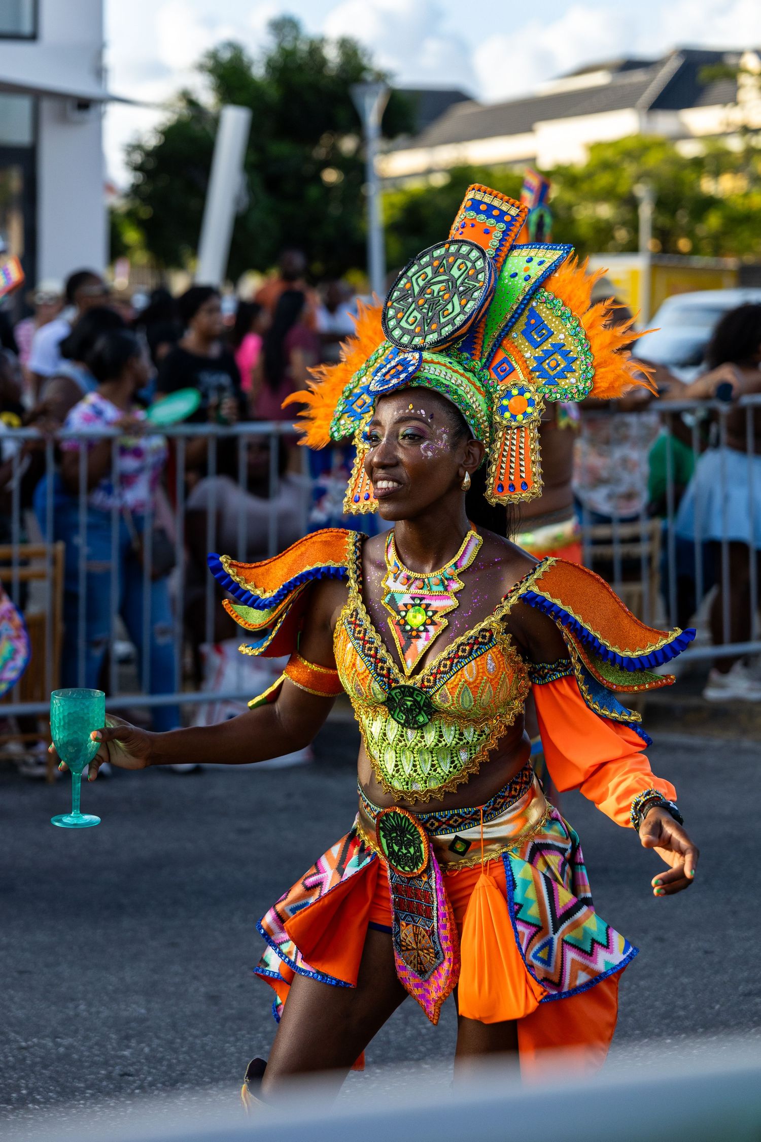 Dancers in vibrant orange and green carnival costumes perform energetic moves during a festival celebration.