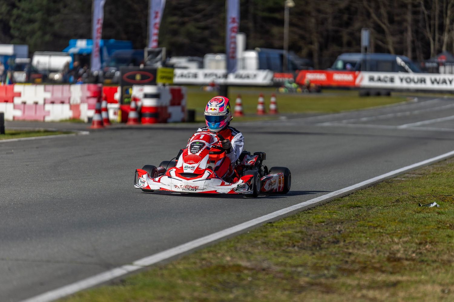 A red and white racing go-kart speeds around a track during a competitive race event.