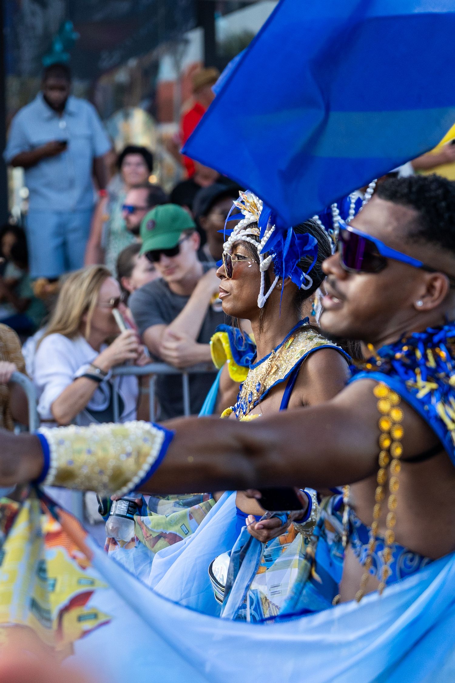 Festival performers in blue and gold costumes dance along parade route with crowd watching.
