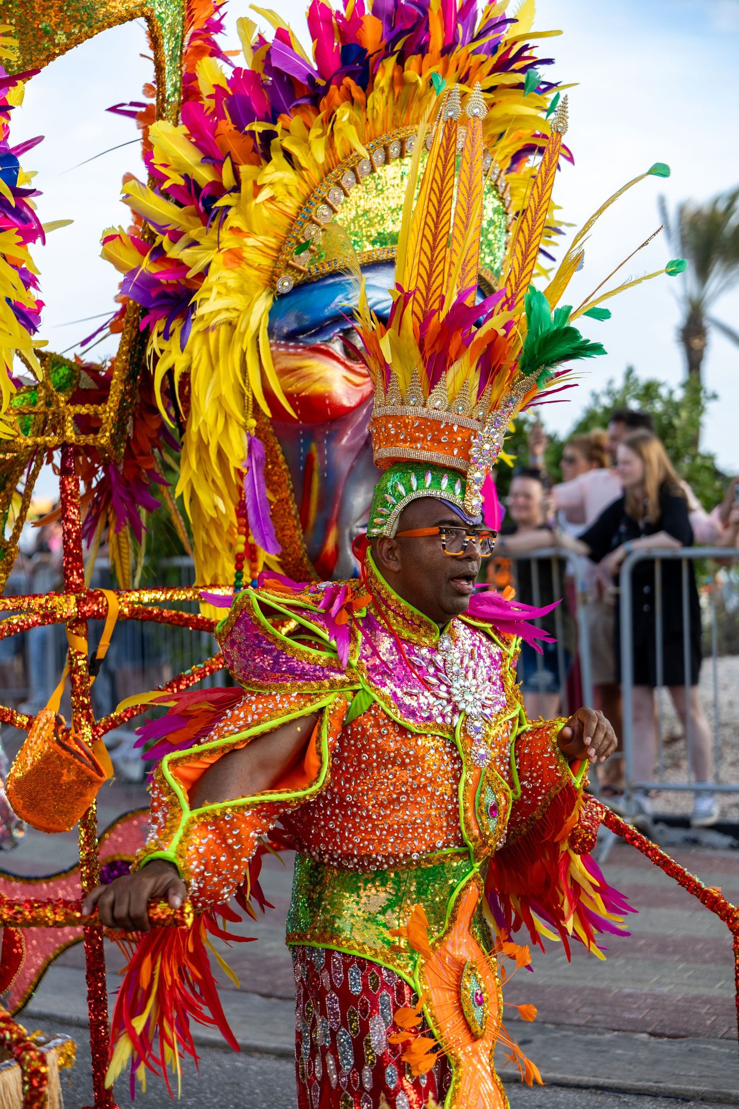 Performer in dazzling orange and yellow feathered carnival costume with intricate headpiece.