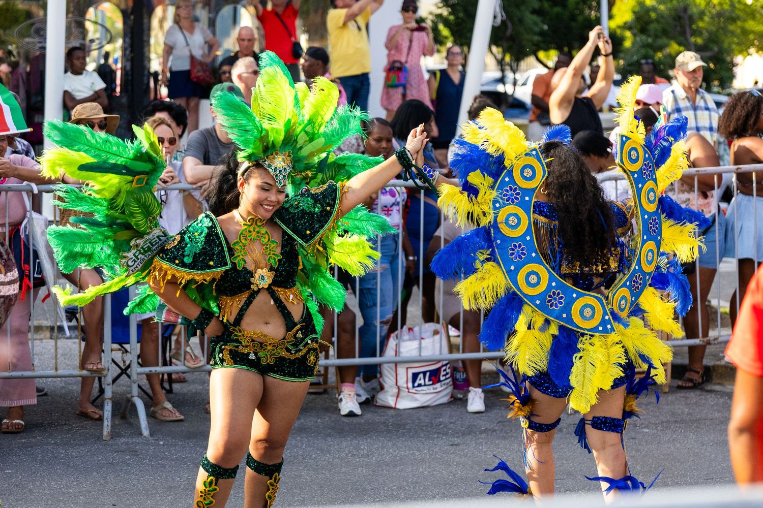Carnival dancers in green and yellow feathered costumes performing choreographed routines.