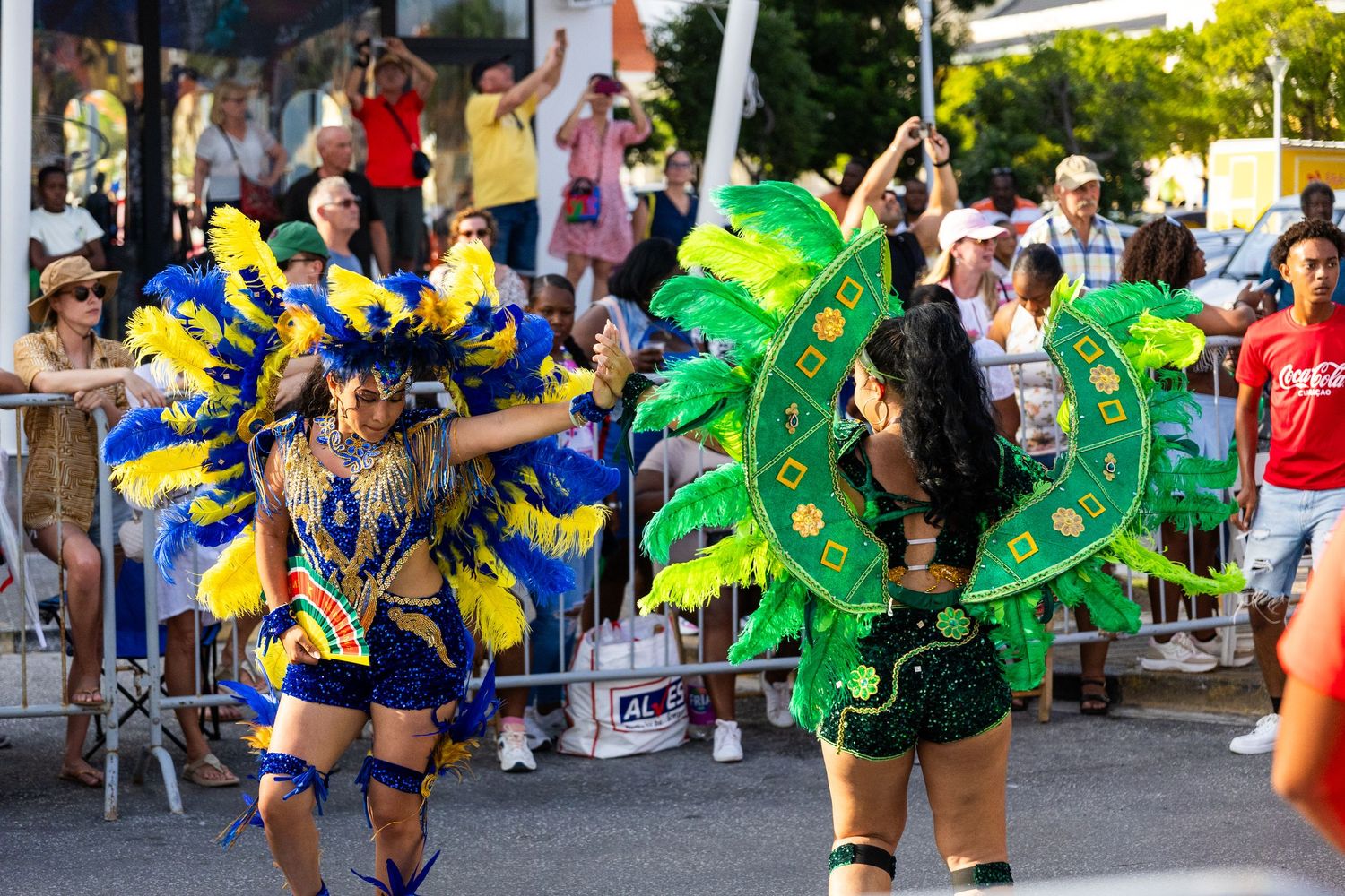 Performers in green and blue feathered carnival costumes dancing along a parade route.