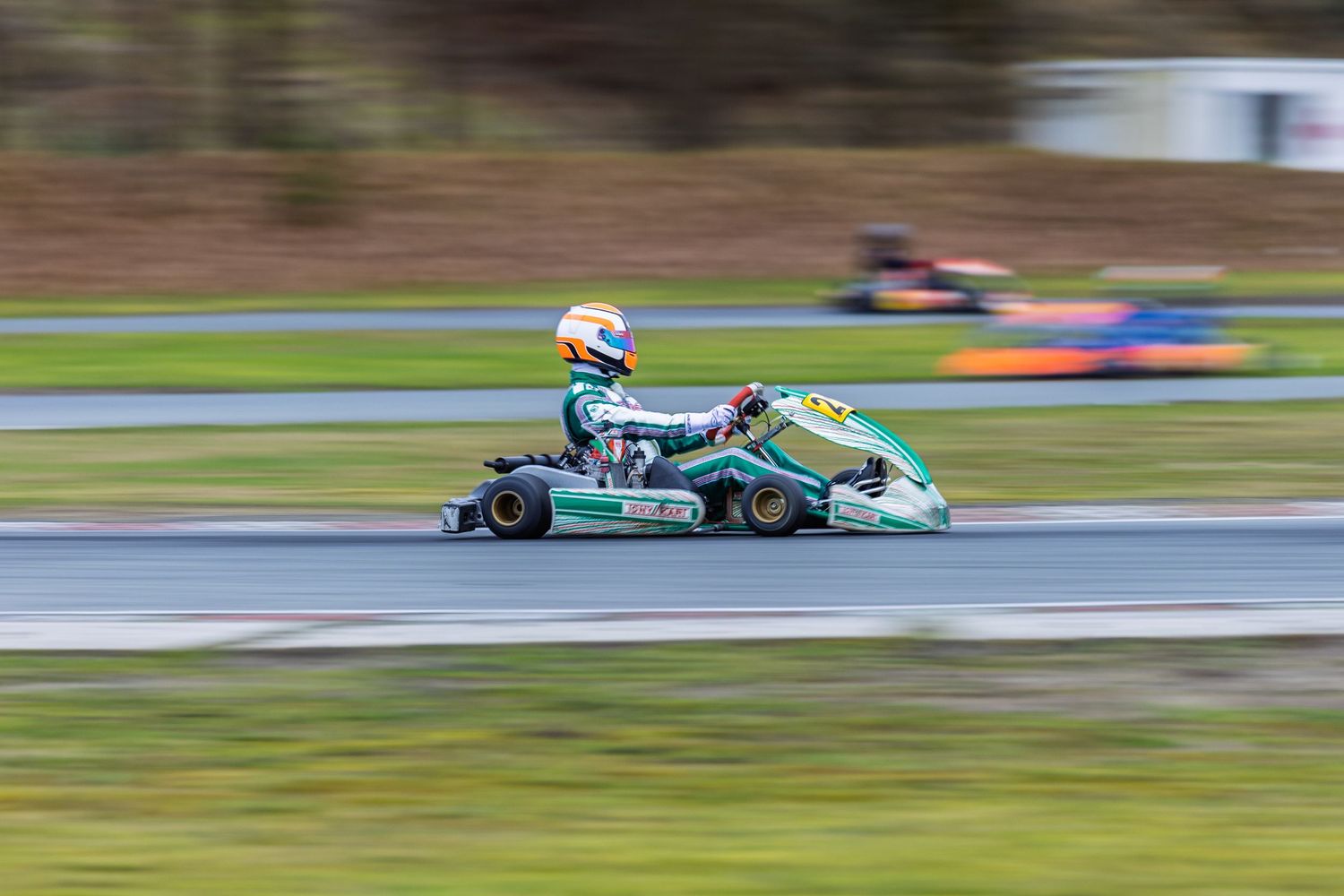 Racing car speeds along a racetrack curve with green and blue livery visible in multiple action shots.