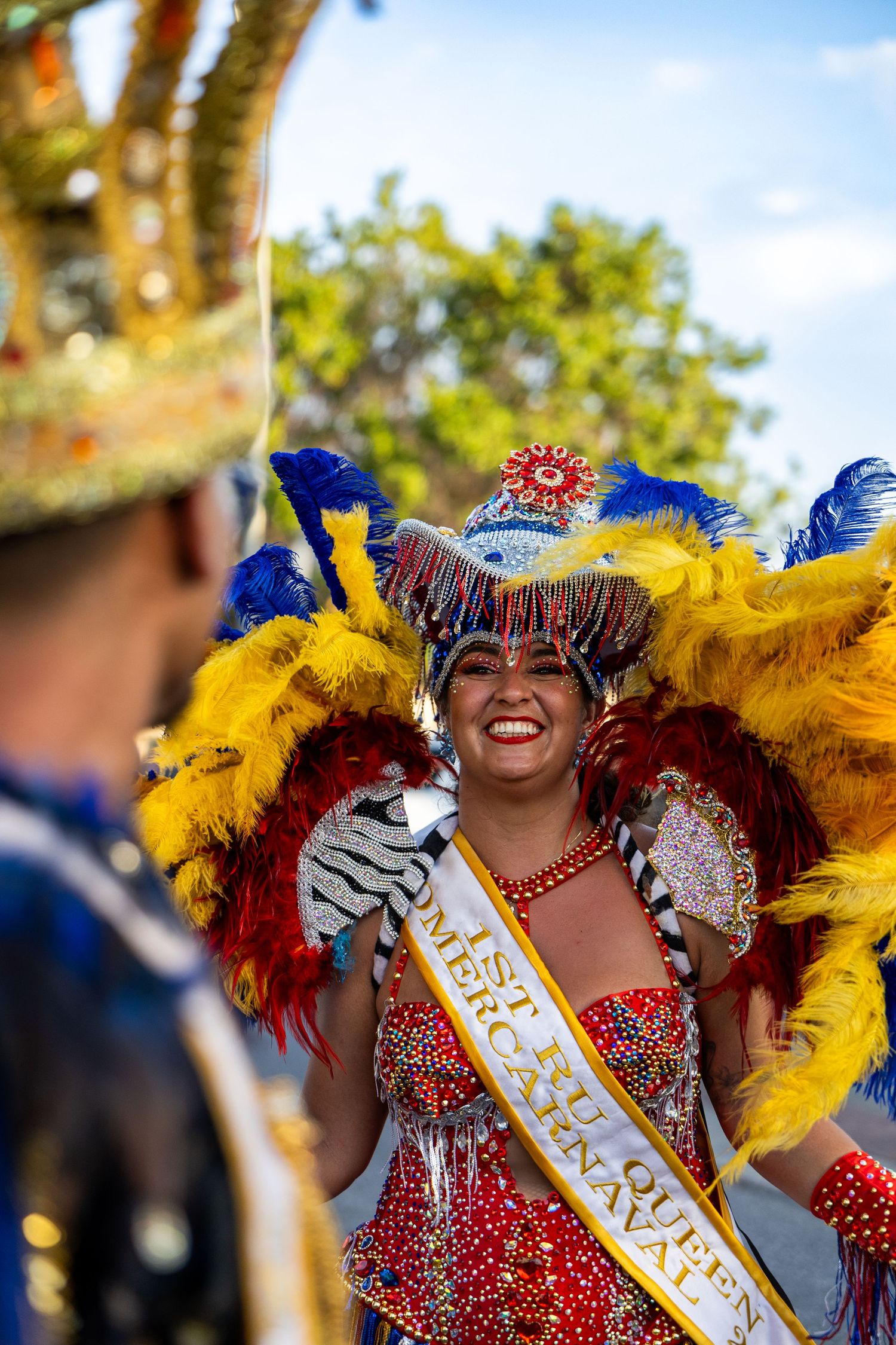 Carnival dancer wearing bright red costume and yellow feathers performs with enthusiasm.