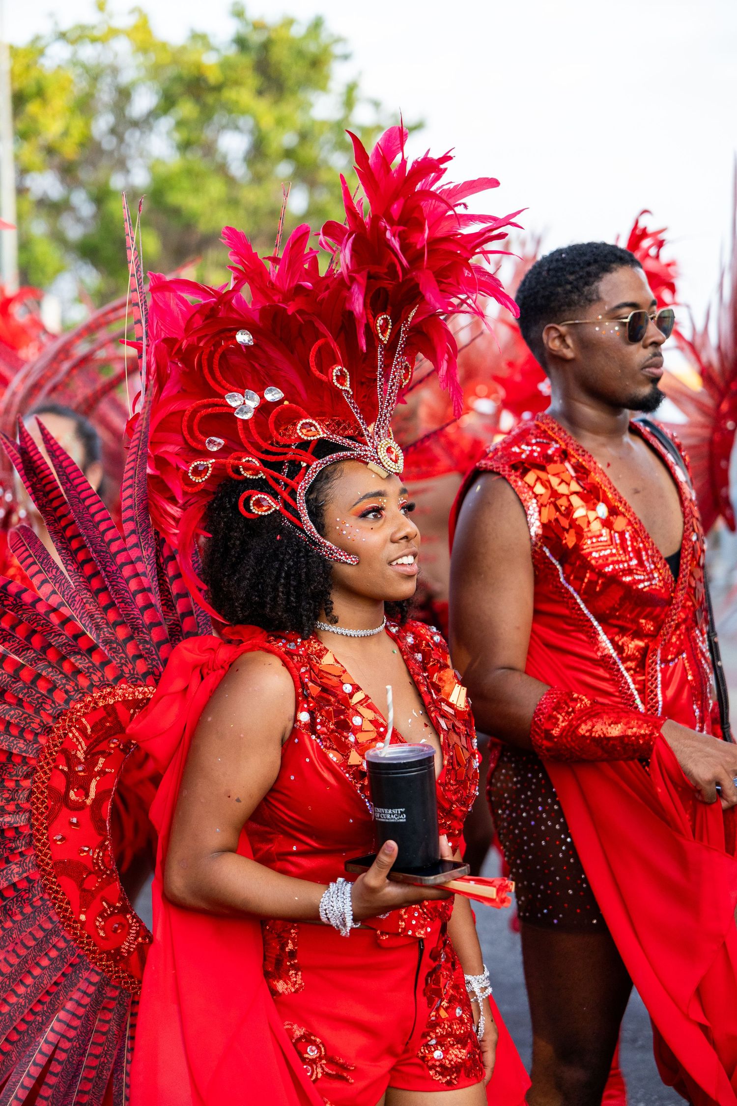 Dancers wearing elaborate red sequined costumes and feathered headpieces line up for a carnival performance.