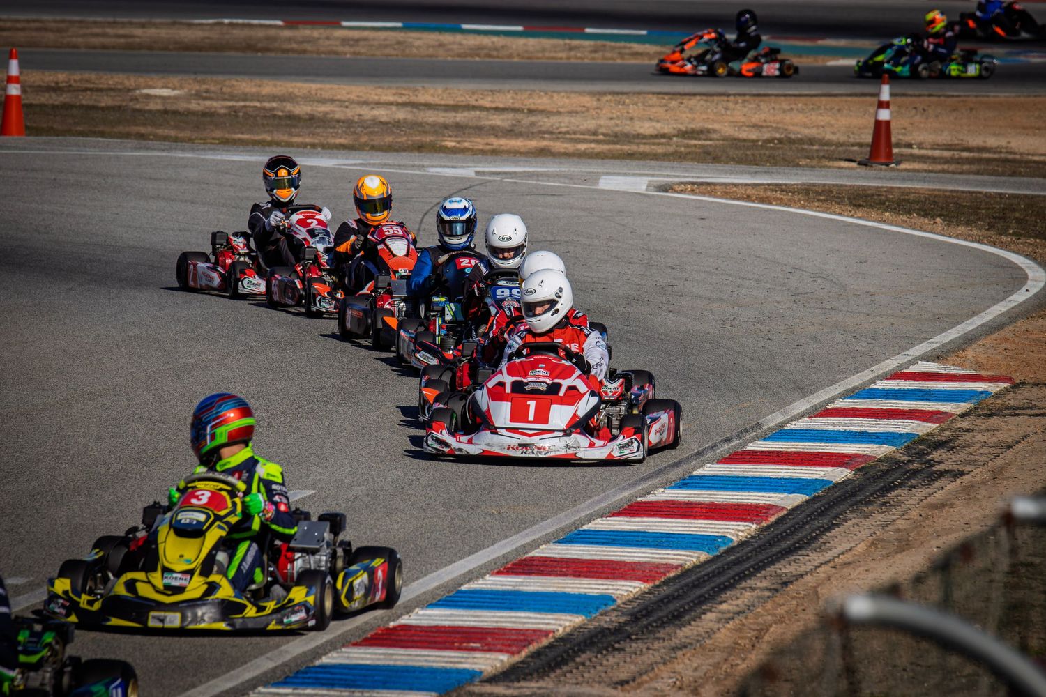 Go-karts battling for position through a challenging corner on a professional racing circuit.