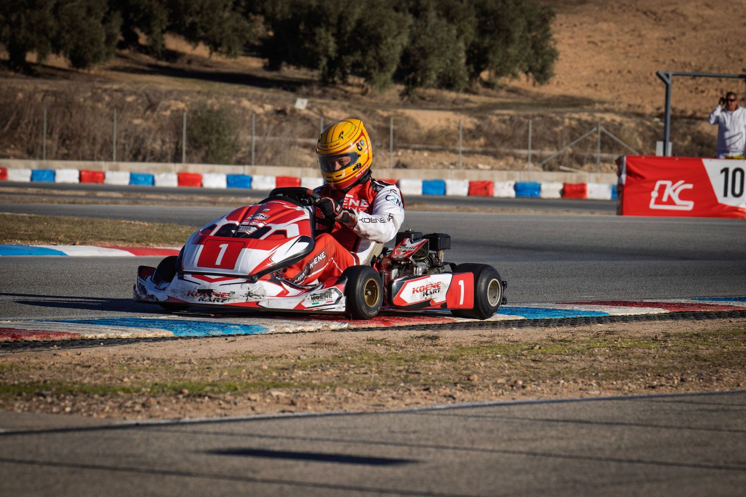 Red racing kart powers through a corner on a professional karting circuit.