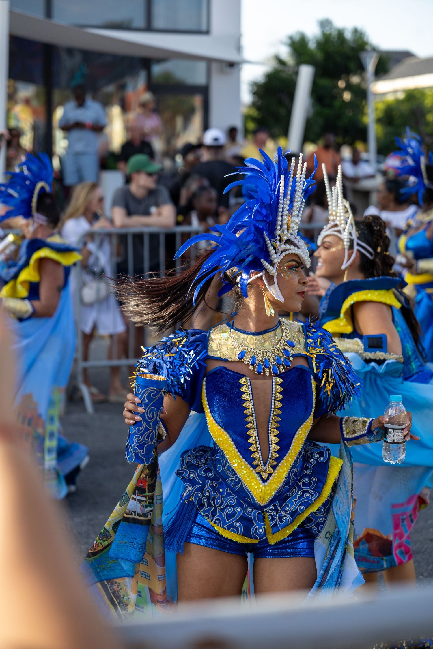 Performers in royal blue costumes with feathered headpieces dance during a street festival.