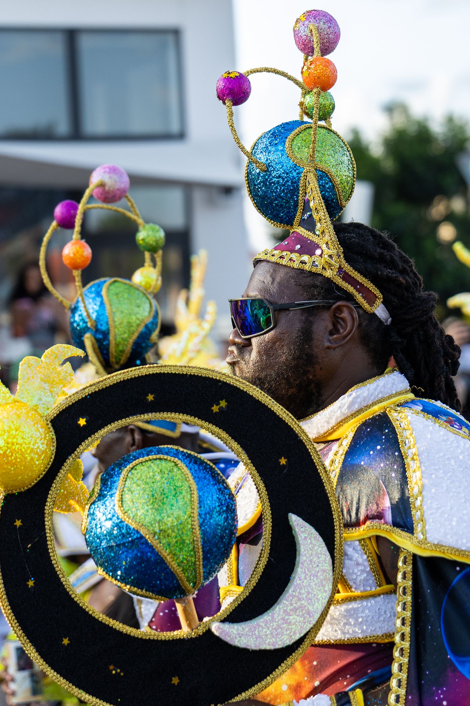 Row of carnival performers wearing glittering blue and gold eye-shaped headpieces.