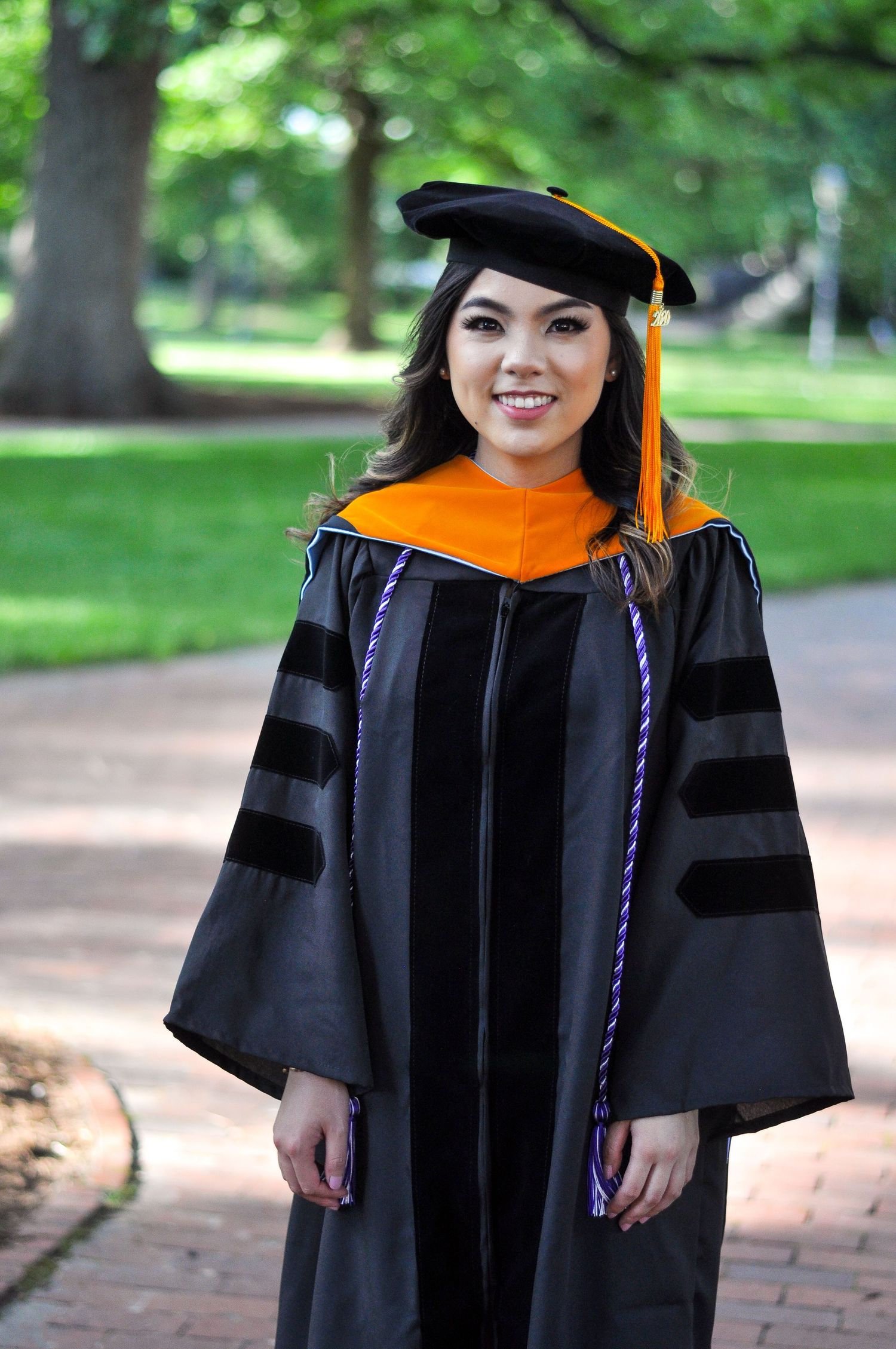 Graduate in traditional black doctoral regalia with orange cap walking on brick pathway.