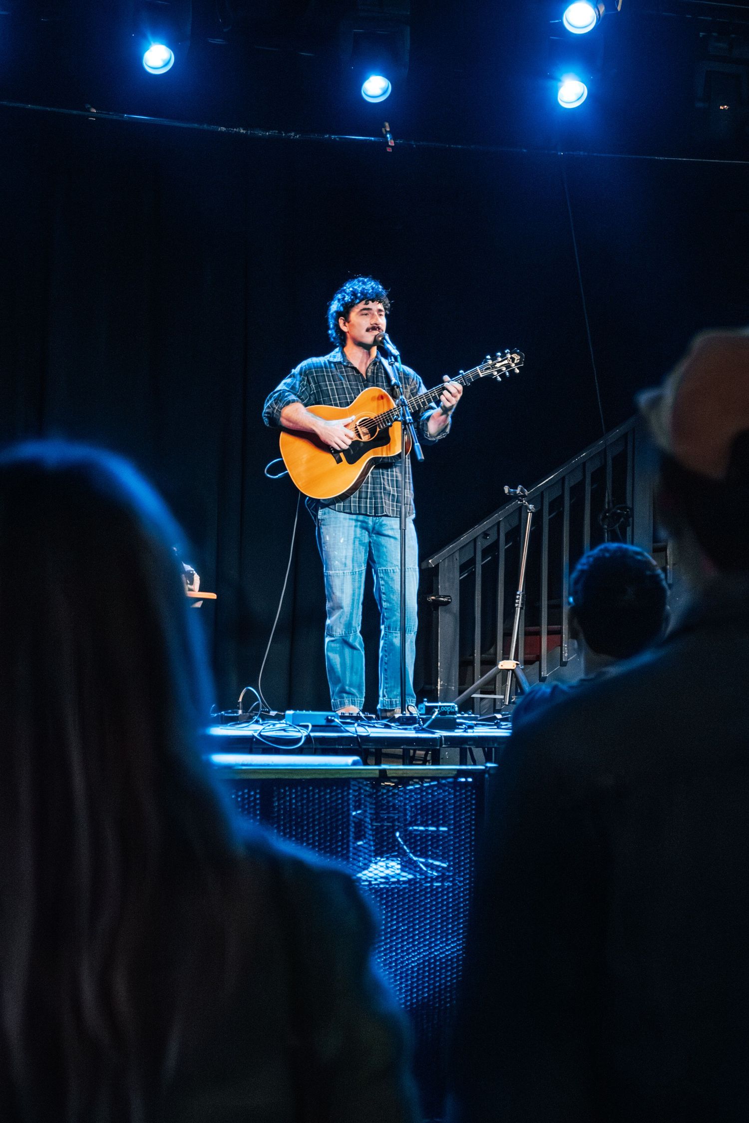 Musician performing on stage under blue spotlights with an acoustic guitar.