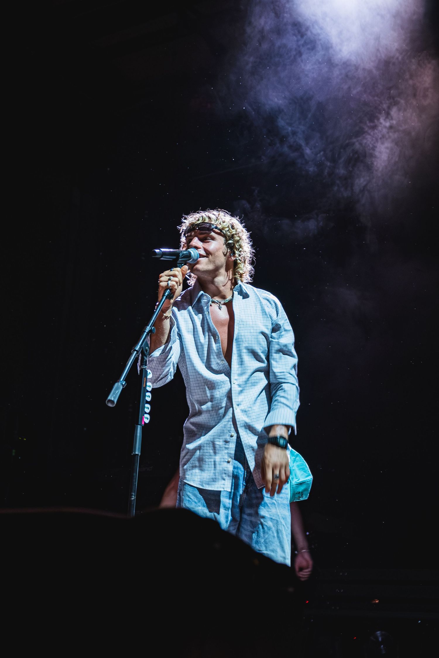 Stage performer in white shirt singing under dramatic lighting and smoke effects.
