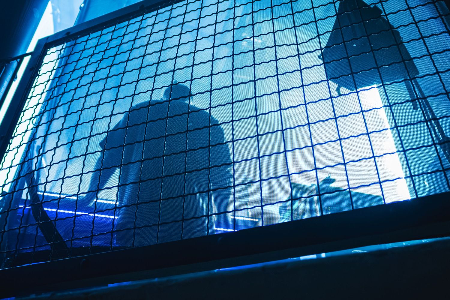 Concert venue ceiling illuminated in blue light with metal grid pattern creating dramatic shadows.