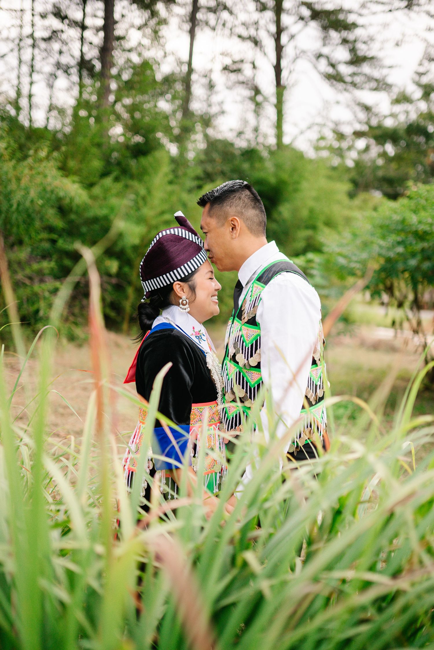 Couple in traditional dress shares intimate moment among tall grass.