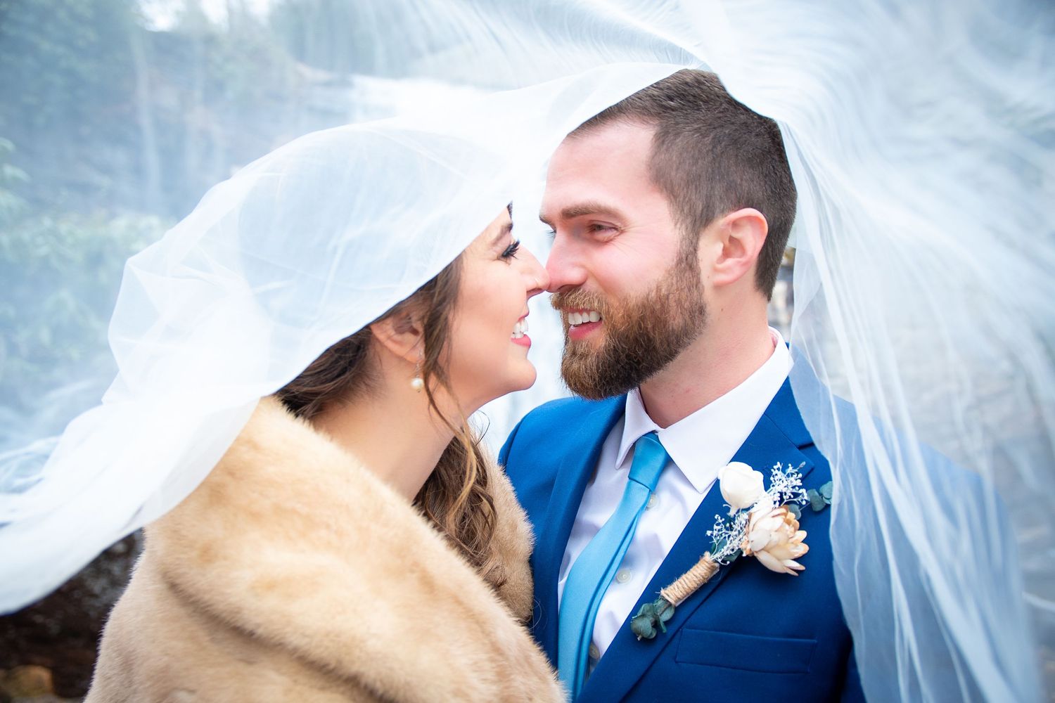 Wedding couple embracing in front of snowy winter backdrop.
