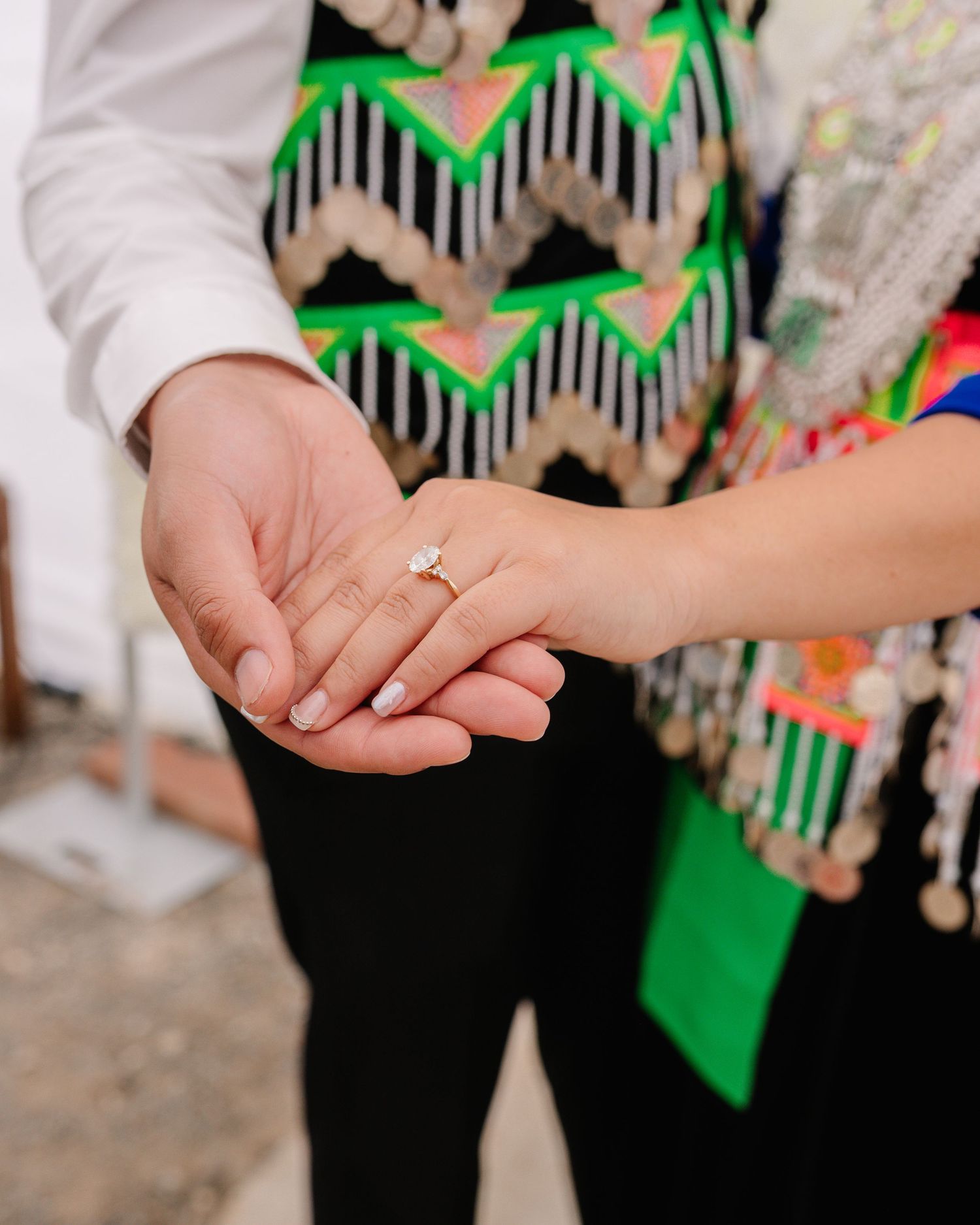 Close-up of hands showing engagement ring against green and black clothing.