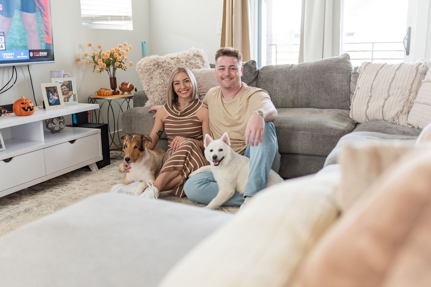 A cozy lifestyle family portrait in a living room, featuring a couple and their two dogs with natural, camera-ready makeup.