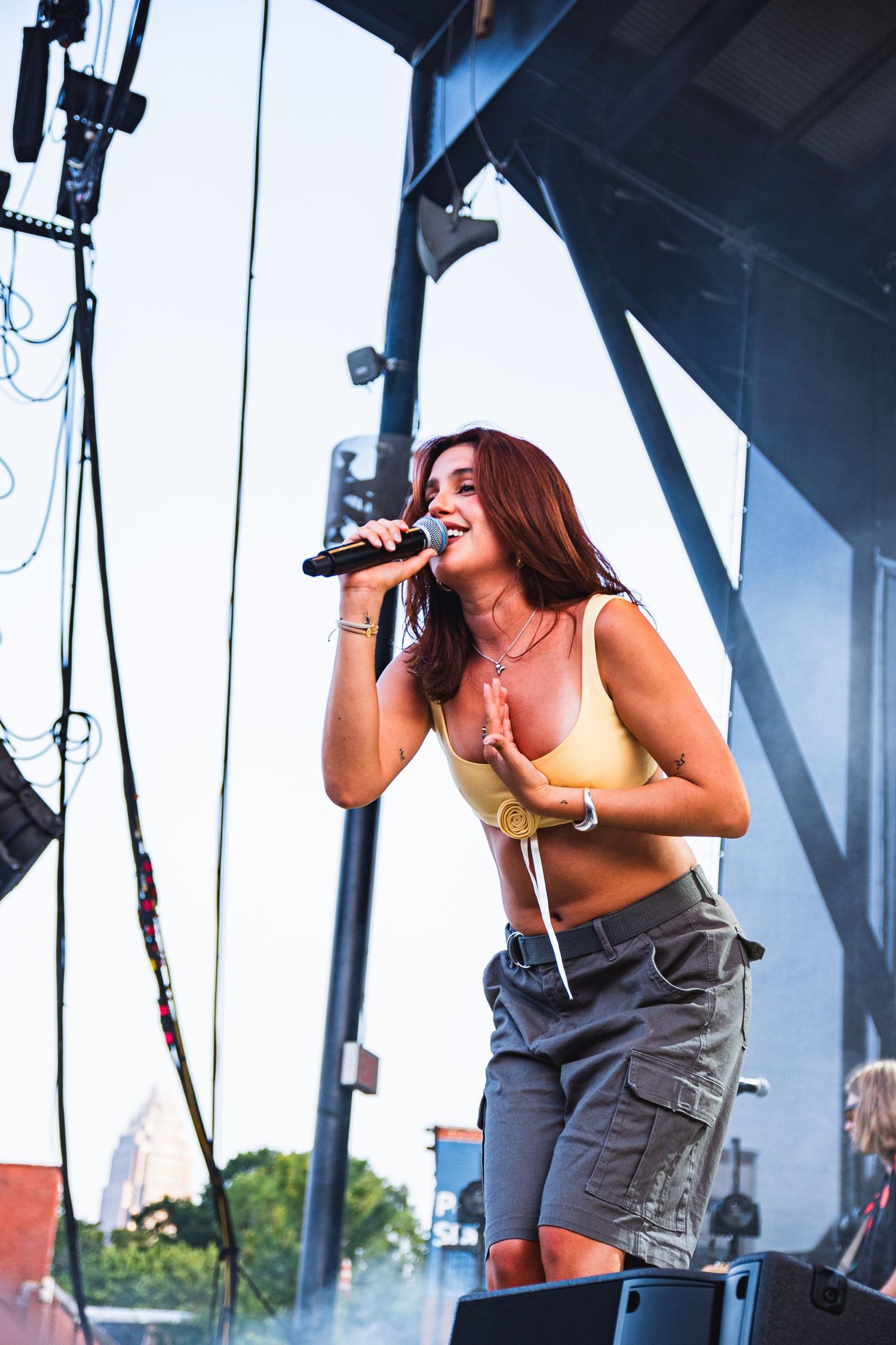 Performer in casual attire energetically singing on outdoor festival stage.