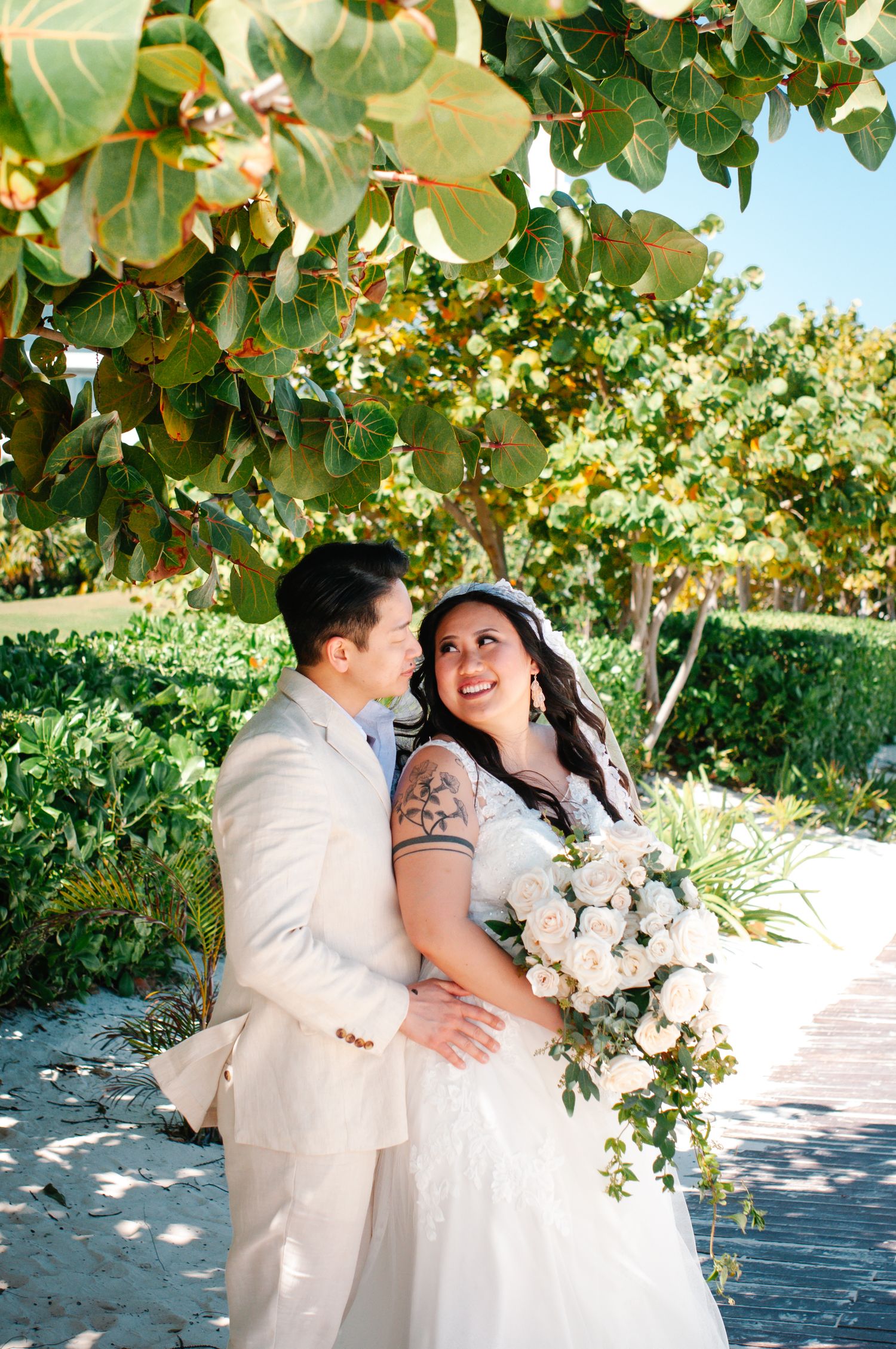 Wedding couple embracing in a sunny garden setting with white floral bouquet.