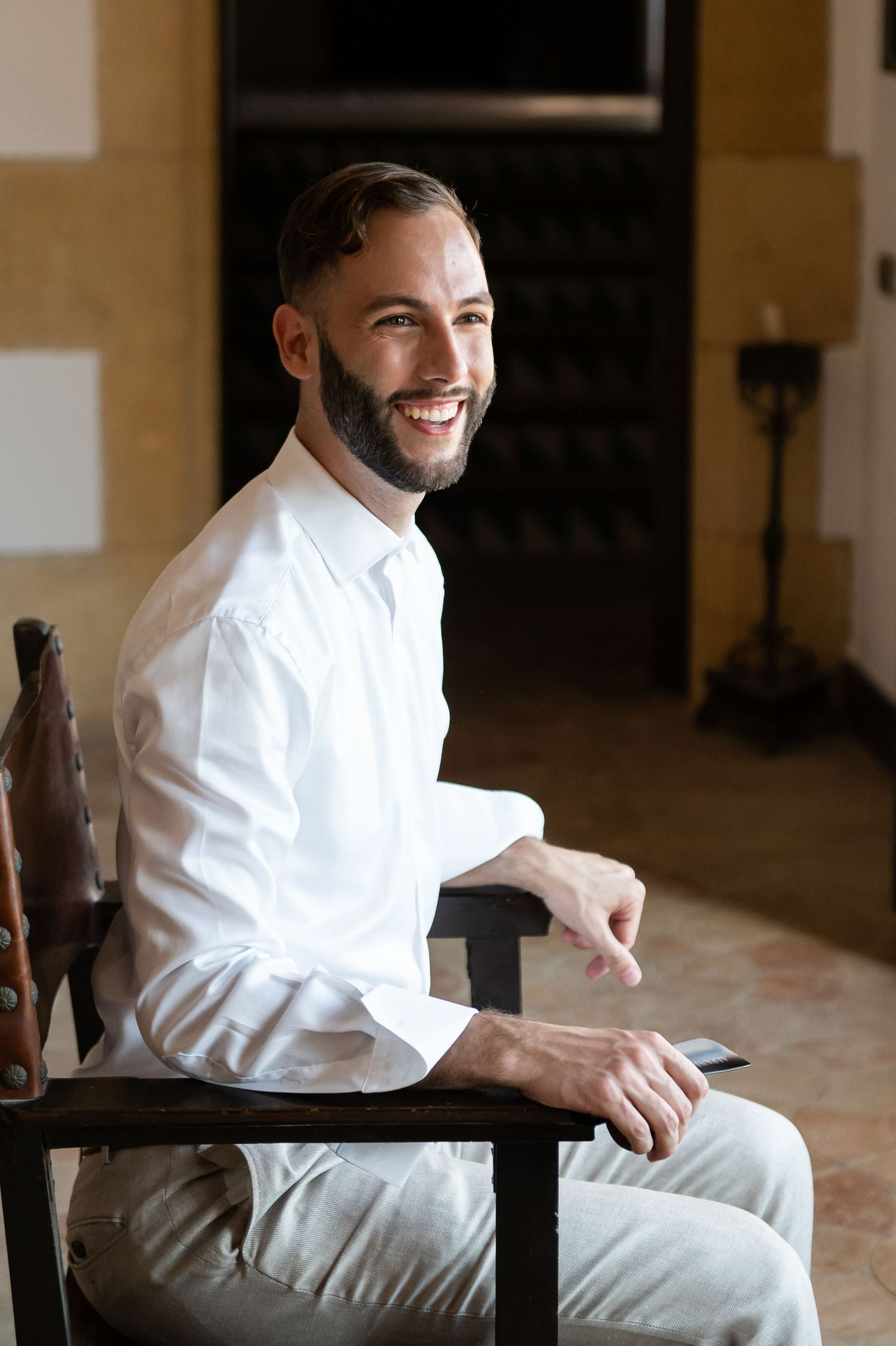Person in white robe sitting and smiling during pre-wedding preparations.