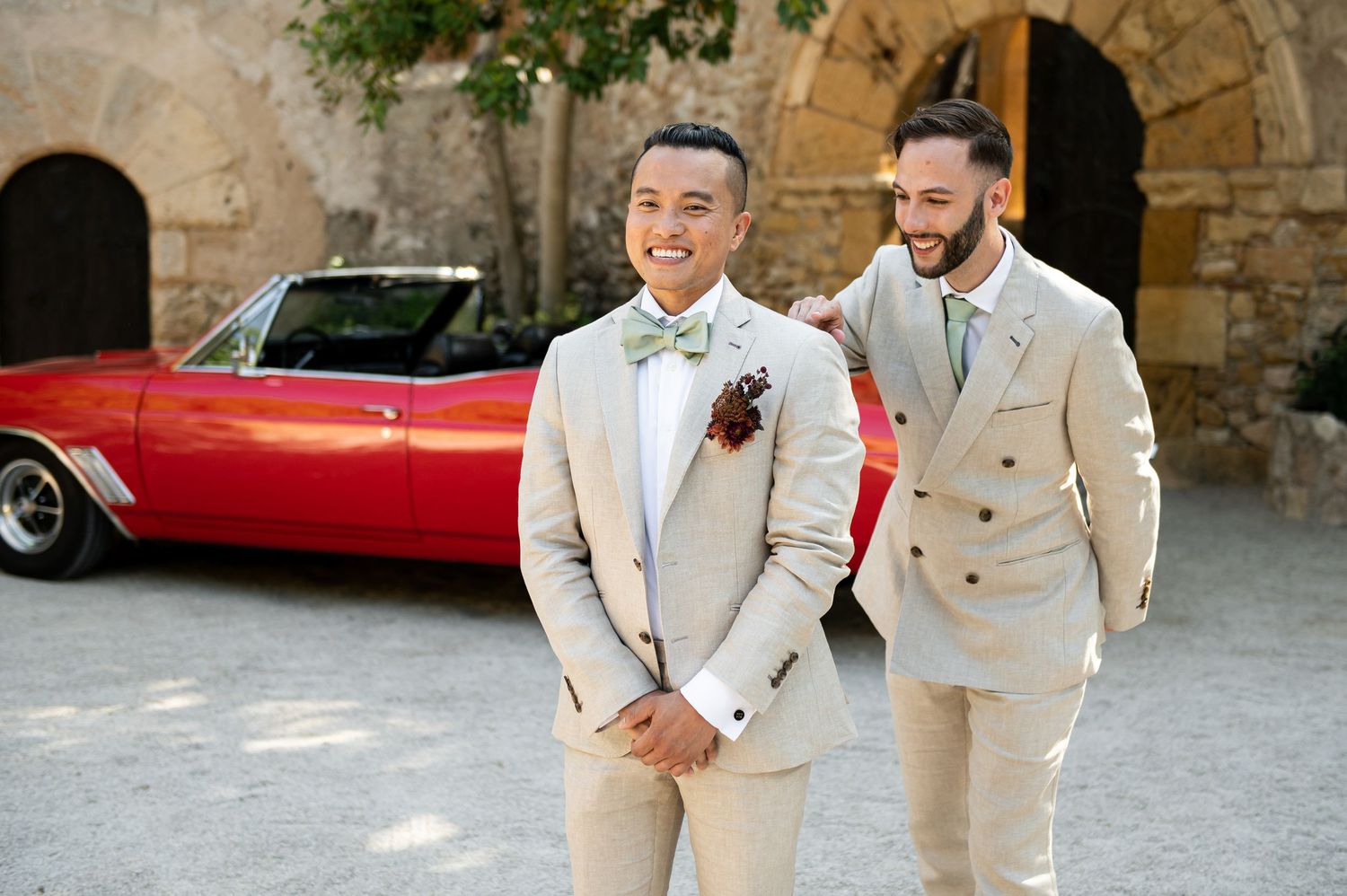 Wedding party in cream-colored suits posing outdoors near stone architecture.
