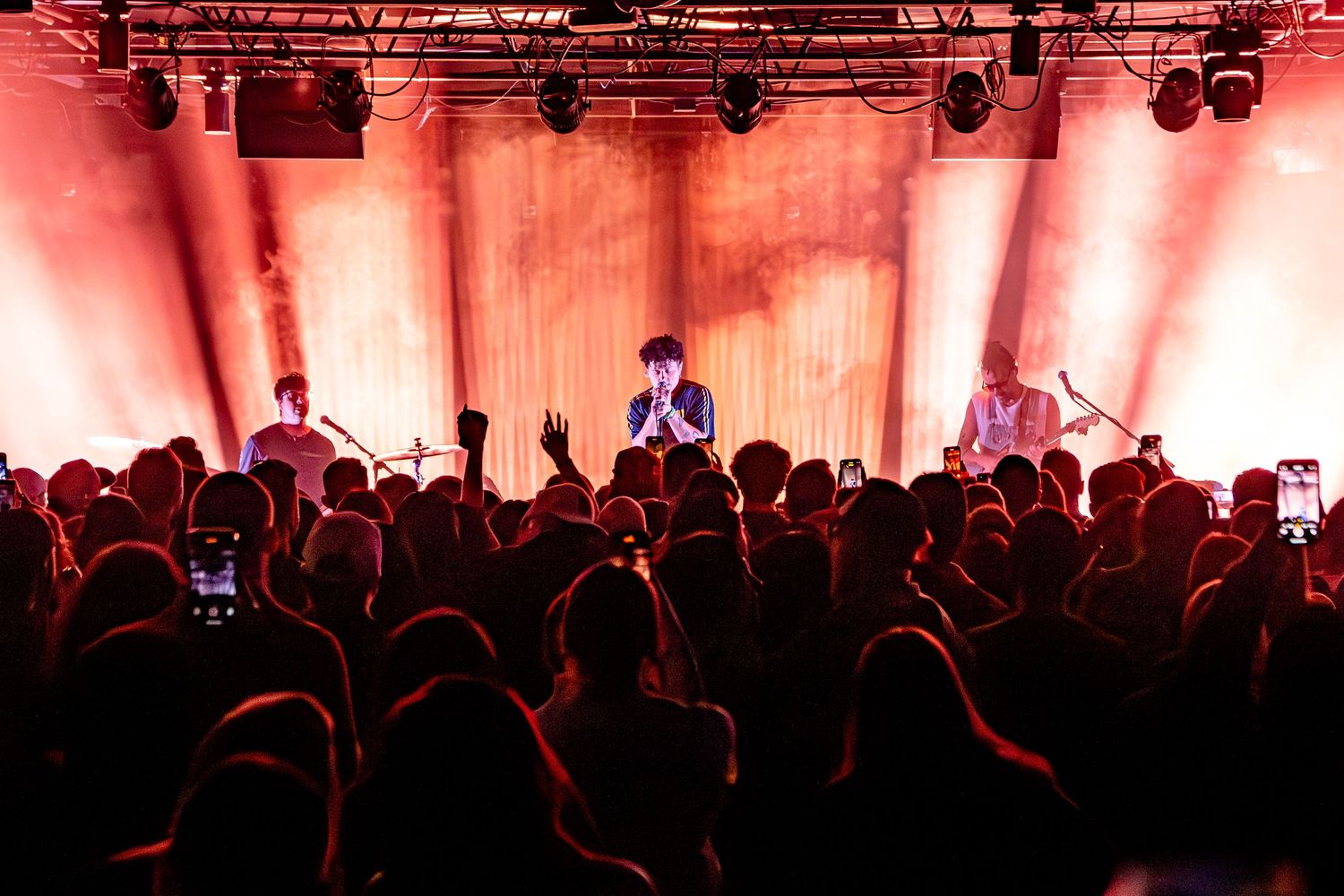 Concert crowd silhouettes against red-lit stage backdrop during live performance.
