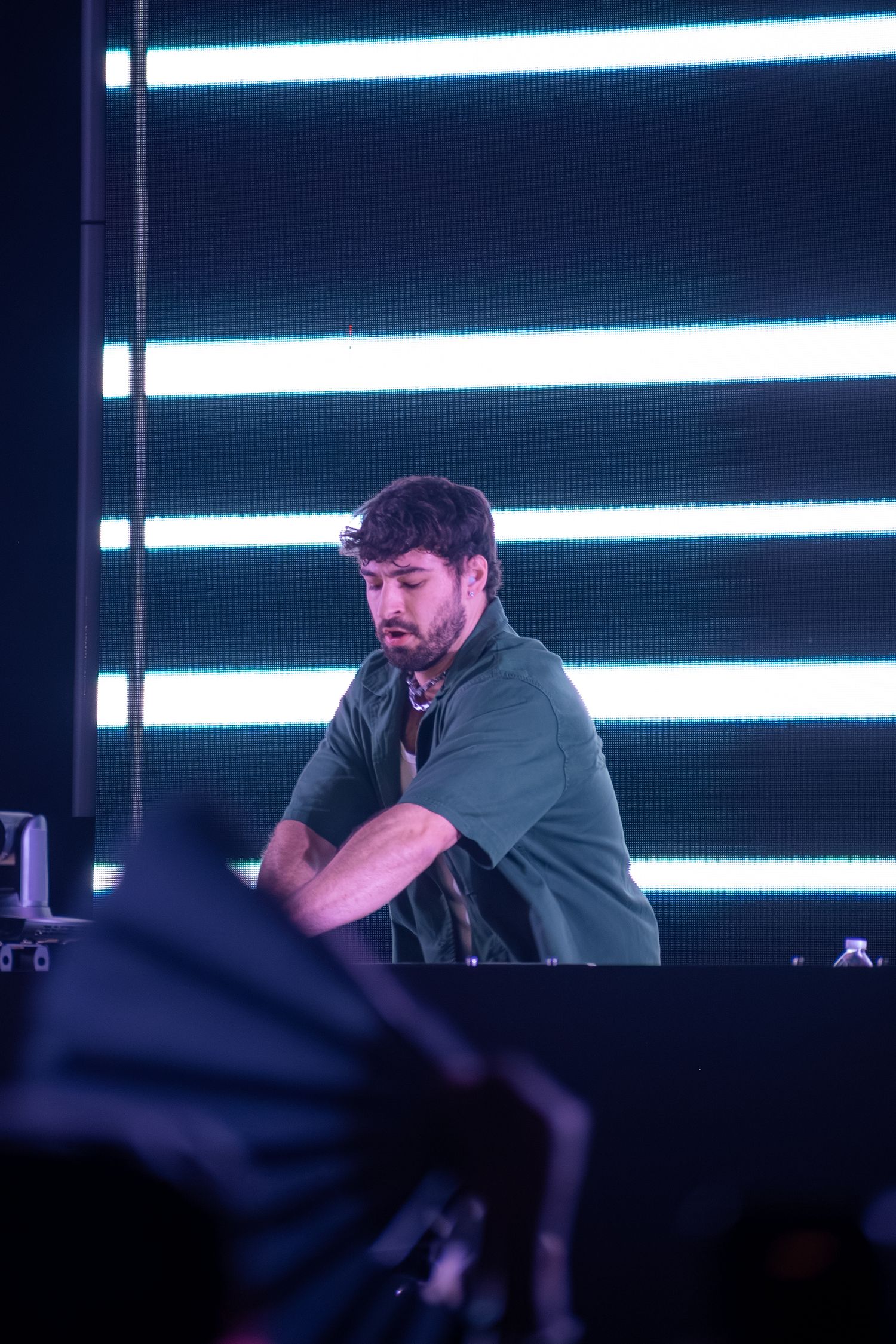 DJ performing at night concert with blue neon light strips backdrop on stage.