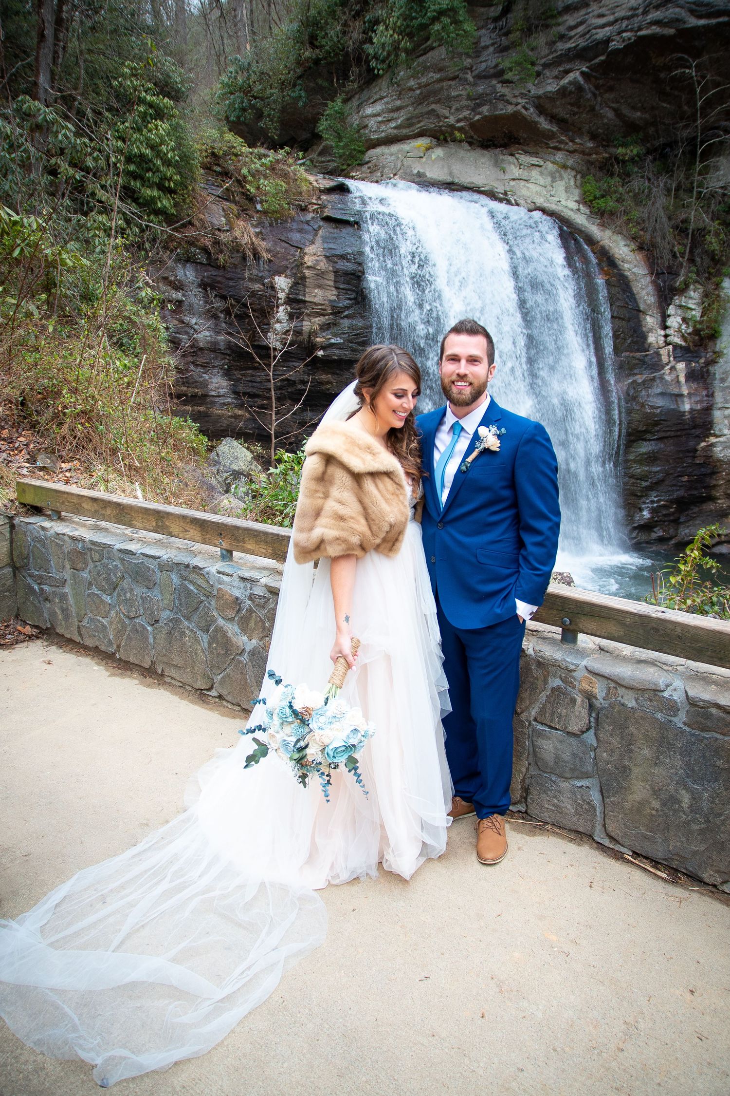 Wedding couple posing together in front of scenic waterfall.