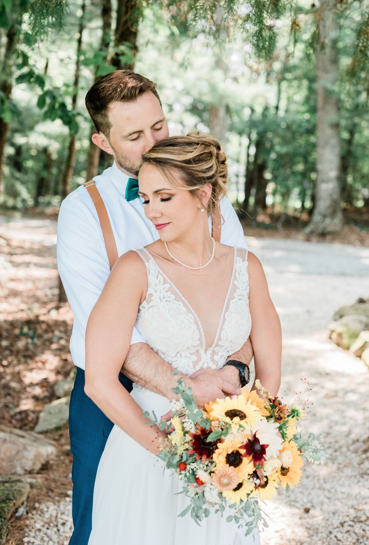 Wedding couple poses with vibrant sunflower bouquet in a romantic outdoor forest setting.