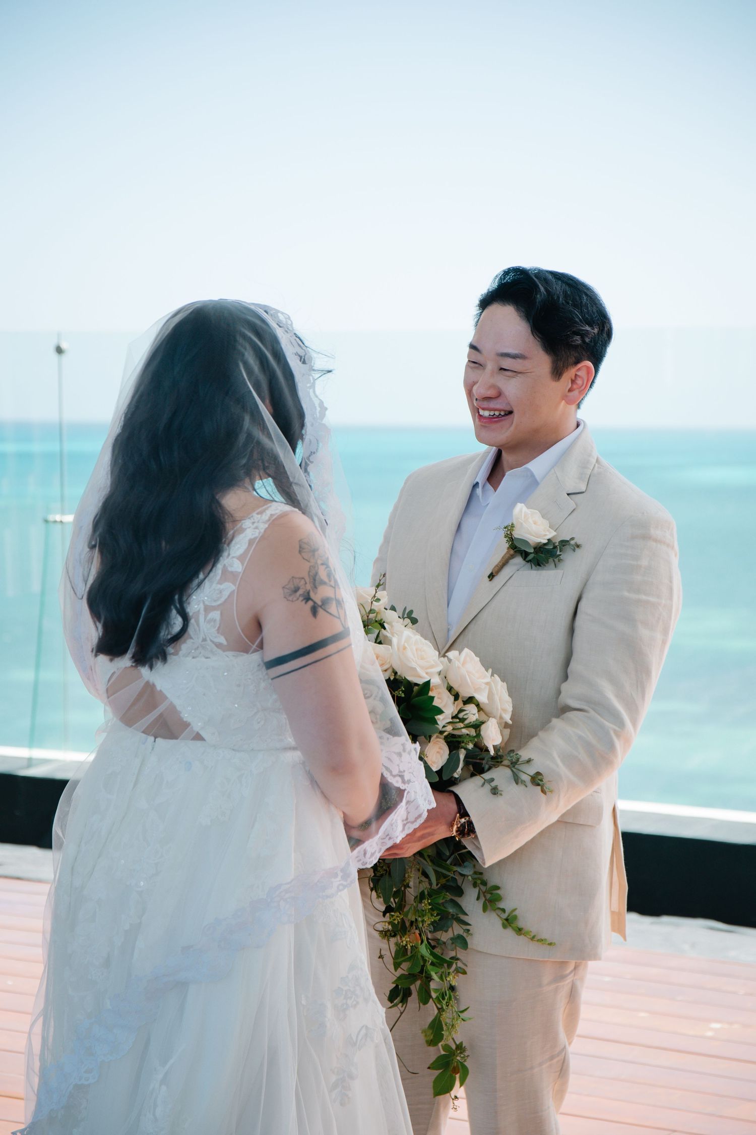 Wedding ceremony on a bright seaside deck with white and floral decorations.