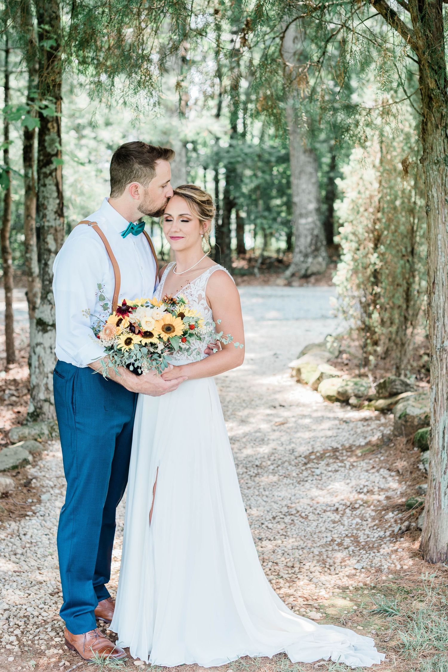 Couple in wedding attire posing together on a tree-lined path.