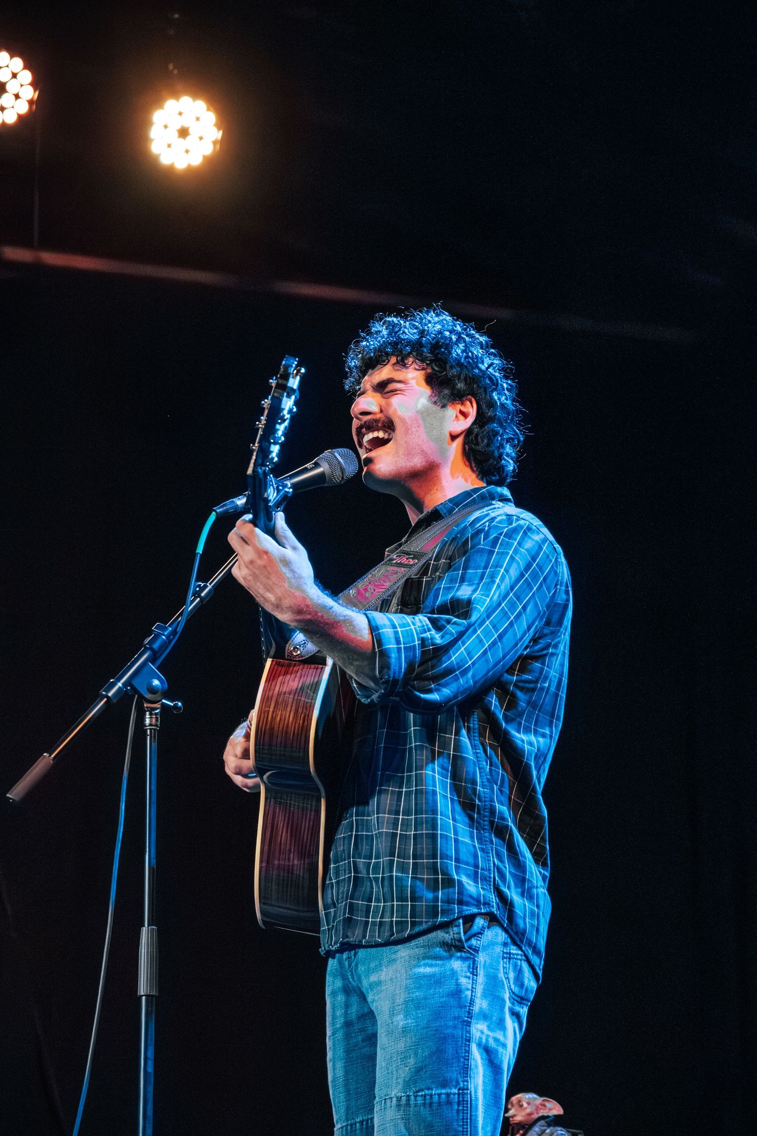 Acoustic guitarist performs on a dark stage with blue lighting effects.