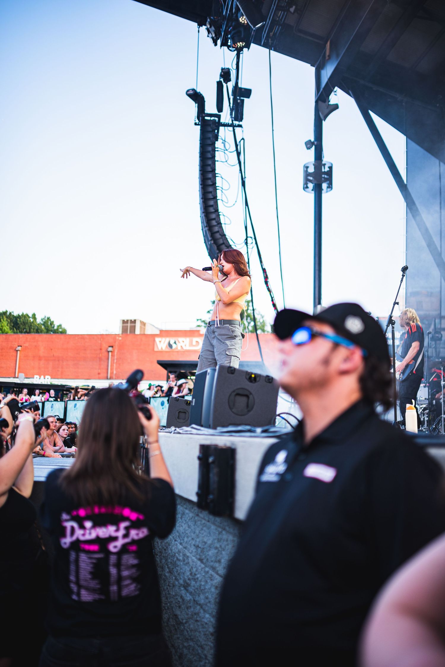 Festival crowd watching outdoor performance with stage equipment visible.