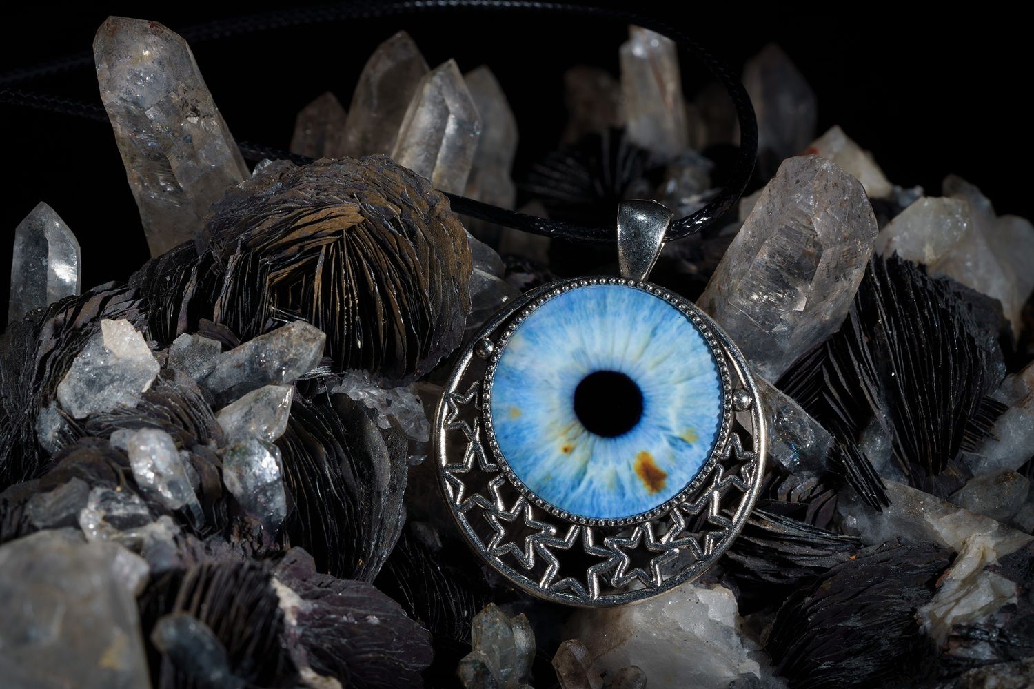 A bright blue glass eye pendant rests among clear quartz crystals and black feathers.