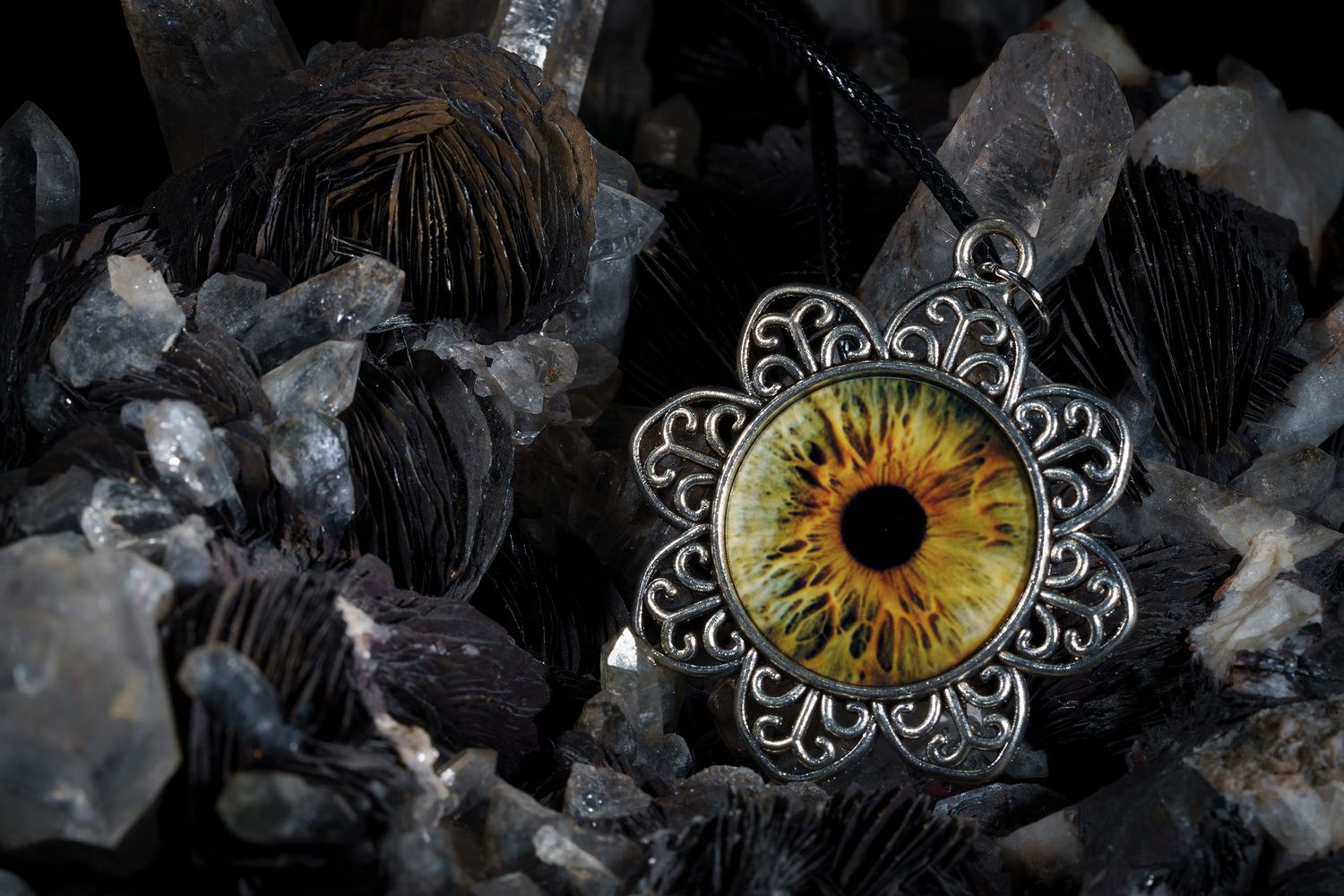 A yellow iris pendant with intricate silver filigree design rests on dark crystals in dramatic lighting.