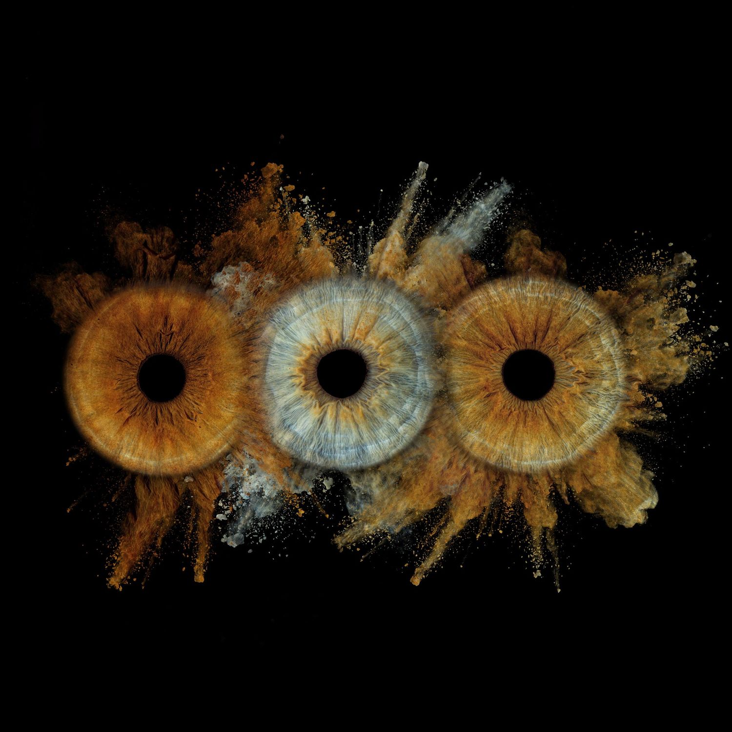 Three human eyes with amber irises surrounded by exploding golden dust particles on a black background.