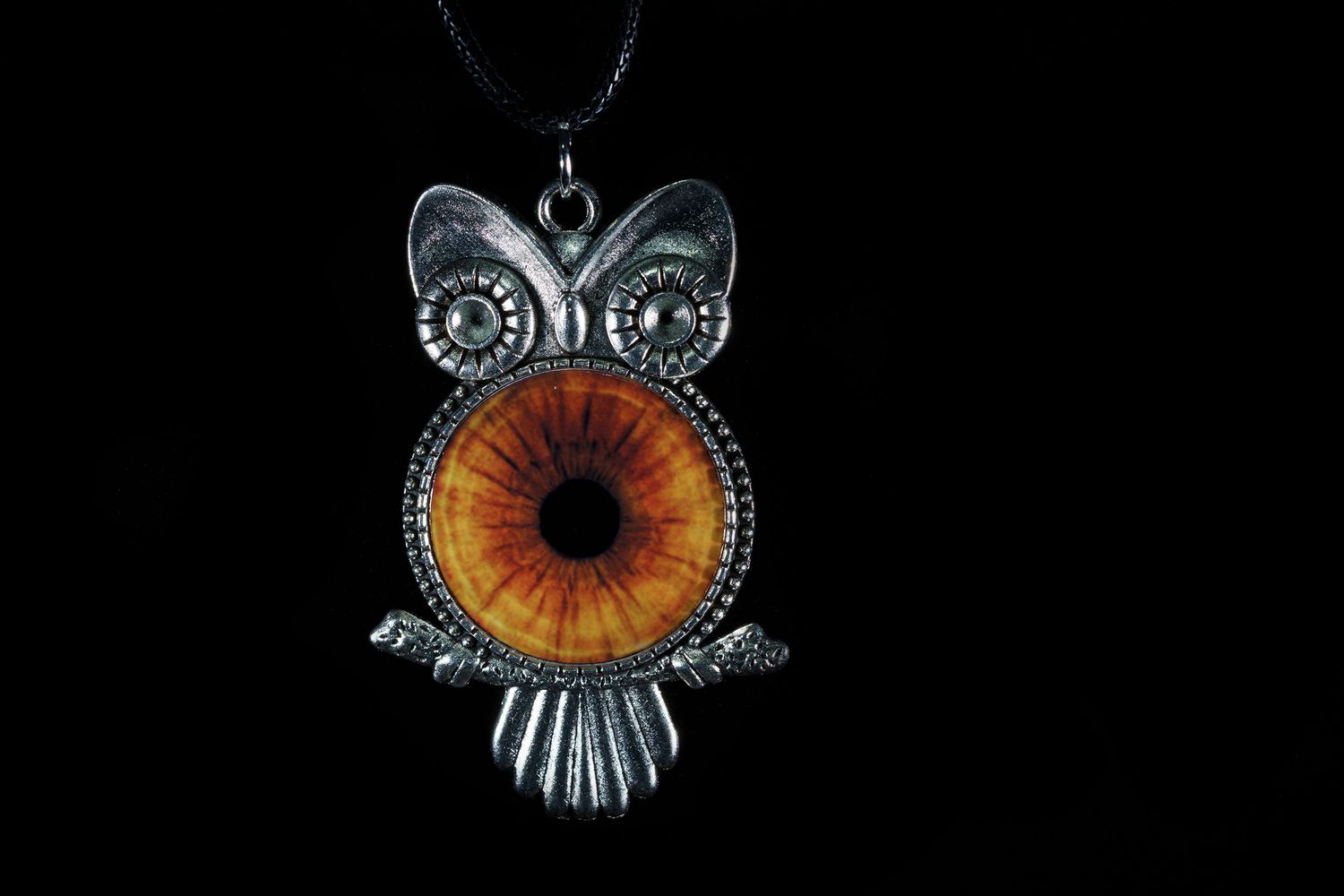An antique silver owl pendant necklace with a large amber colored glass eye on black background.