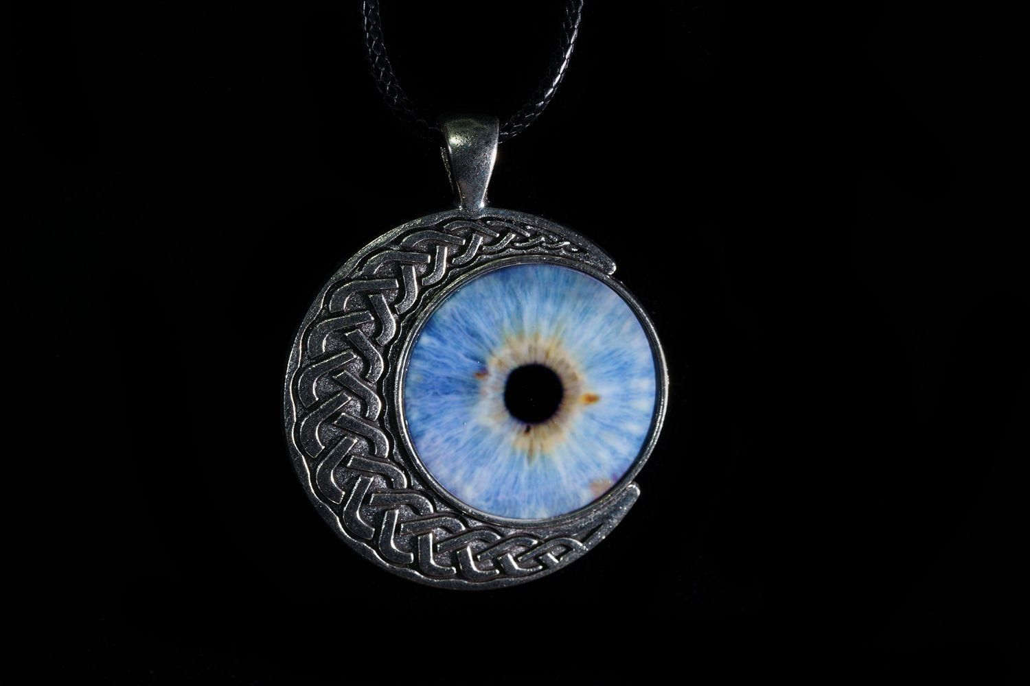A crescent moon pendant necklace featuring an iridescent blue glass eye design against a dark background.