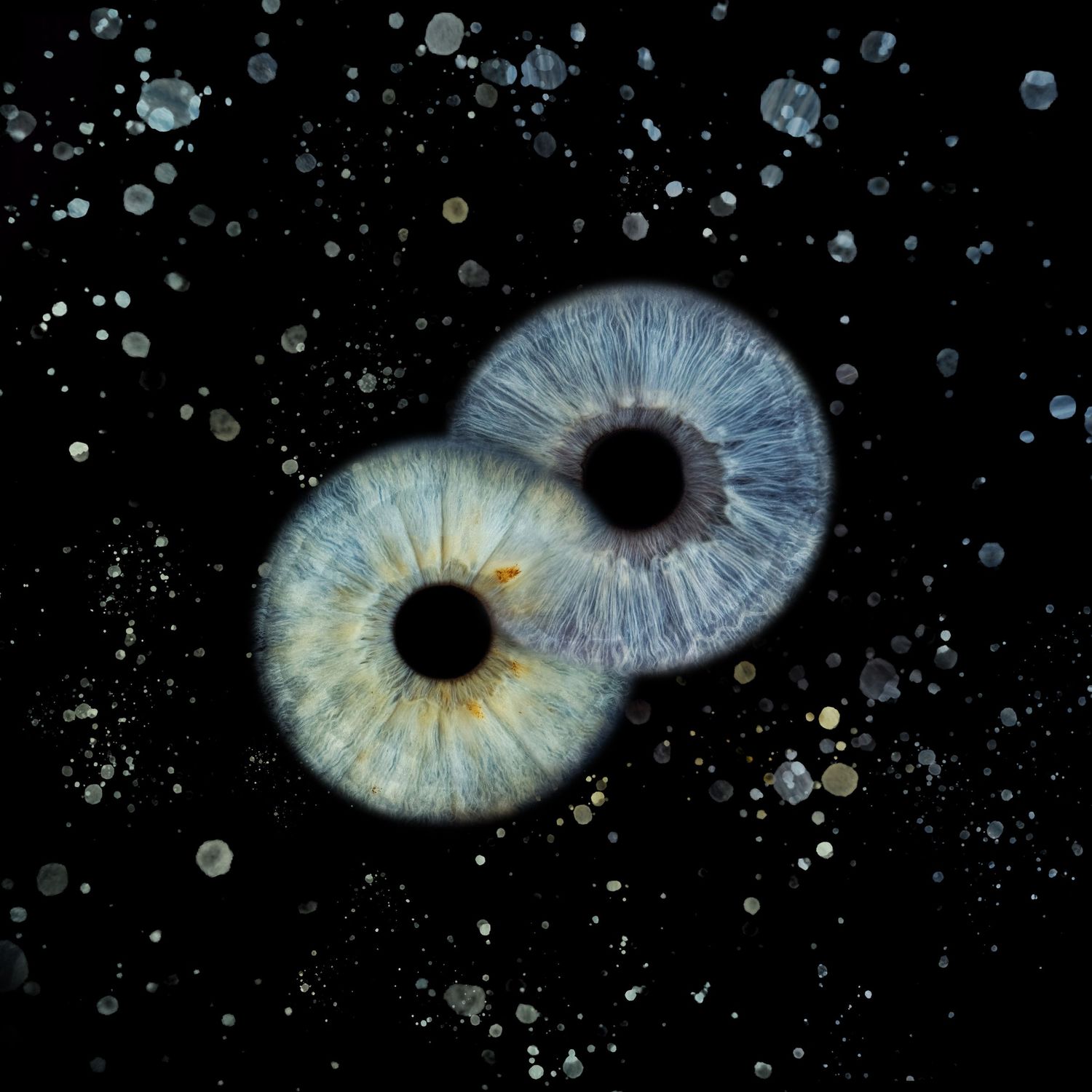 Two overlapping human irises with blue and green hues against a dark starry background, resembling galaxies in space.