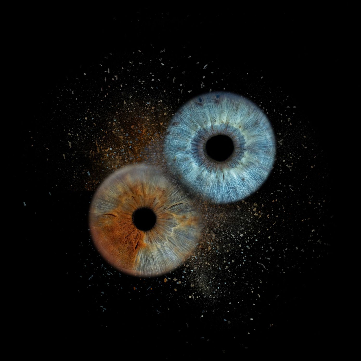 Two human irises, one amber brown and one blue, floating with golden dust particles on black background.