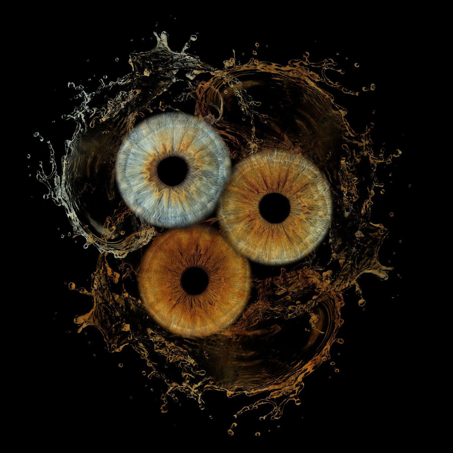 Three human irises with blue and brown tones surrounded by a dramatic liquid splash on a black background.