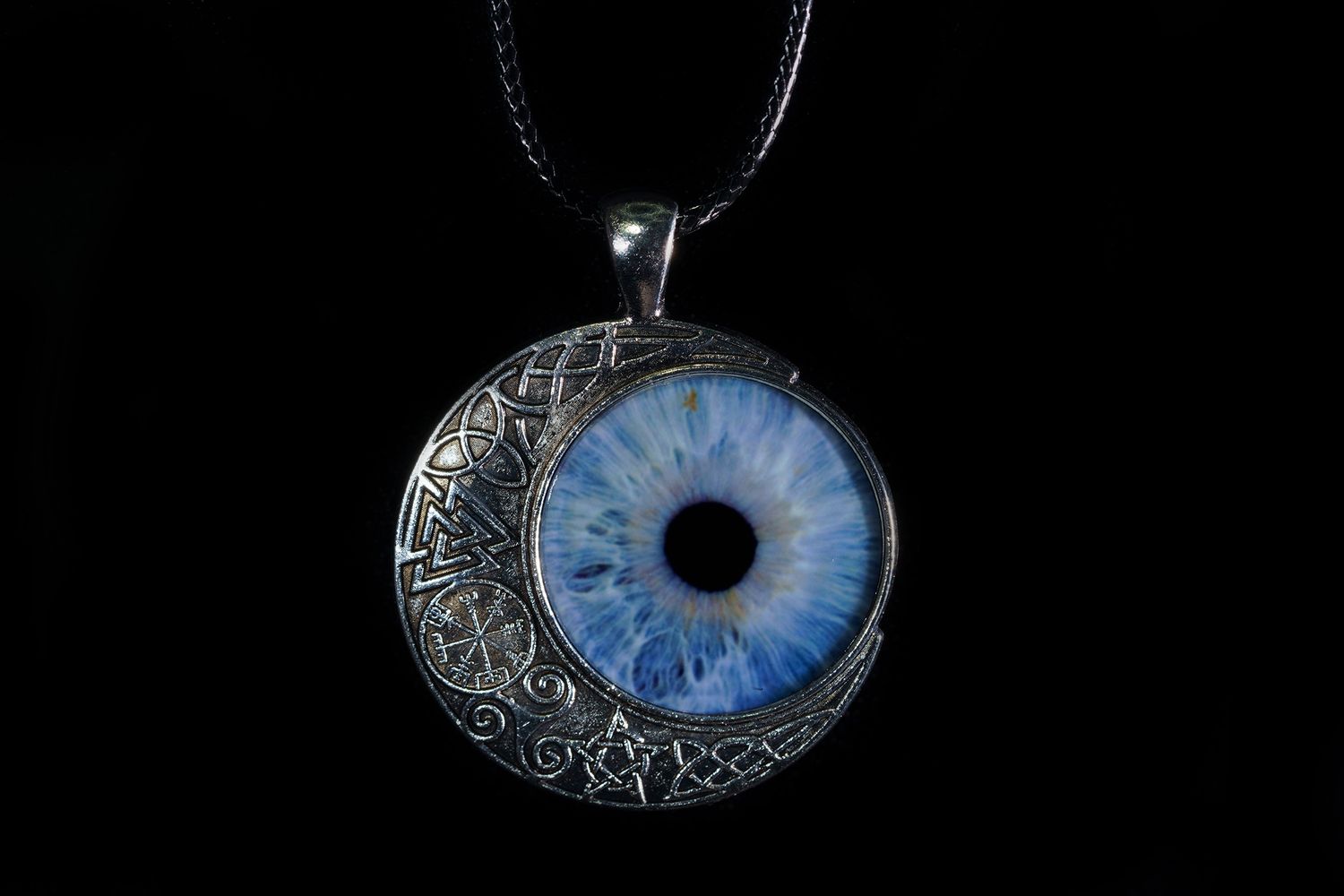A silver crescent moon pendant necklace with a detailed blue eye design against a black background.