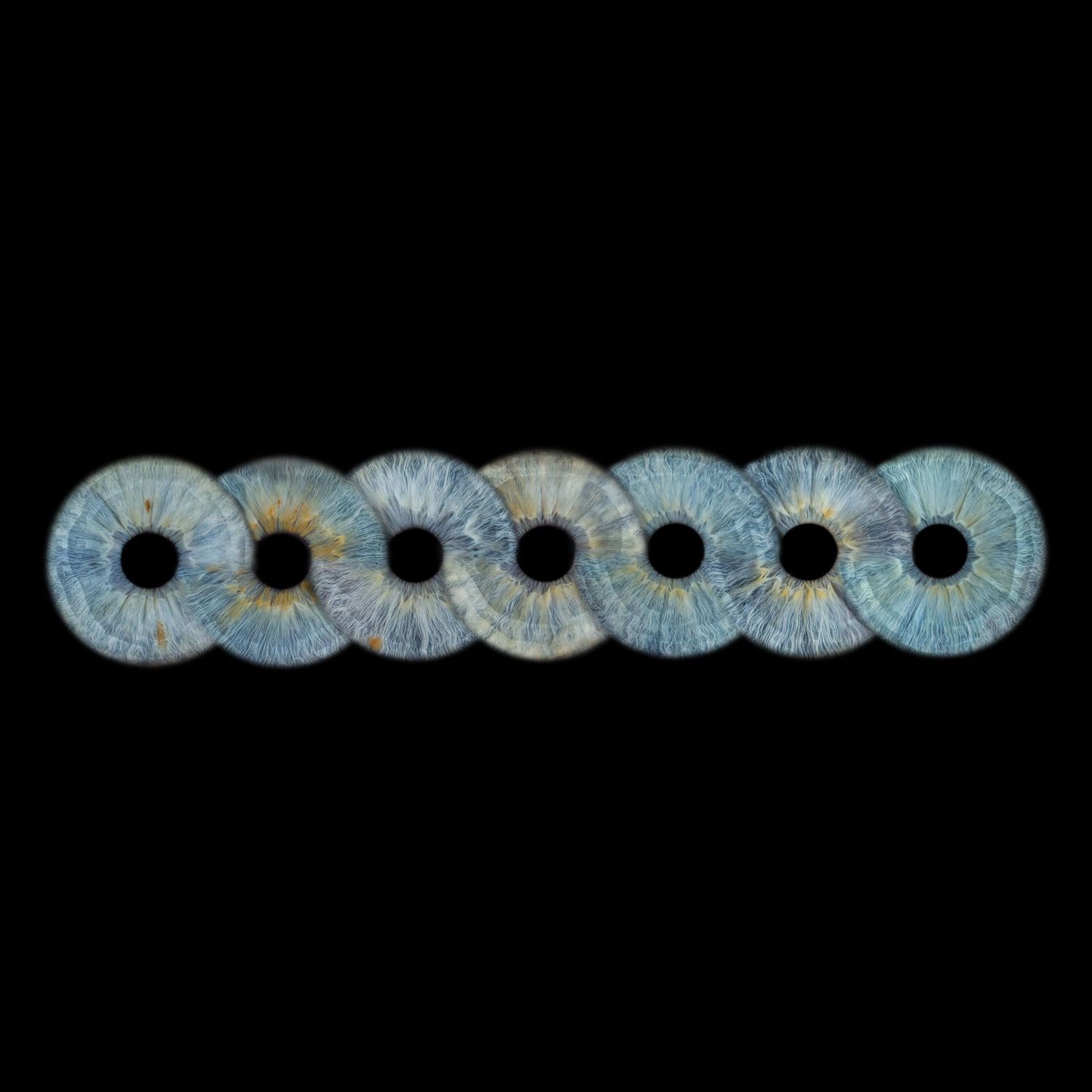 Seven blue human irises arranged in a horizontal row against a black background, showcasing intricate eye detail.