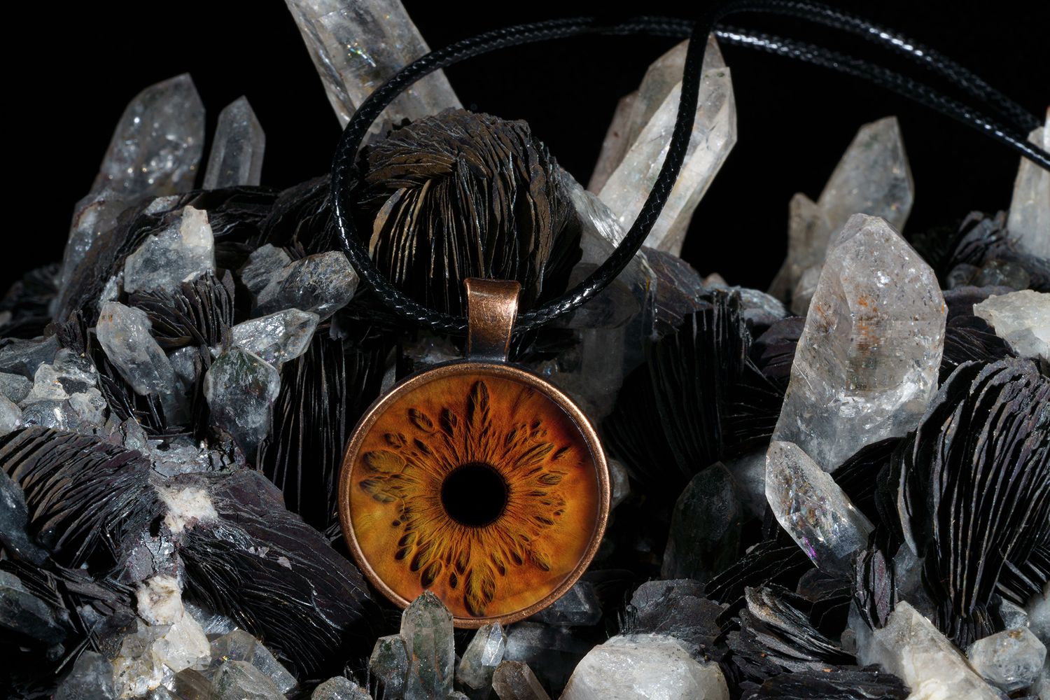 Handcrafted circular amber pendant with floral design rests on raw crystal quartz points and black stones.